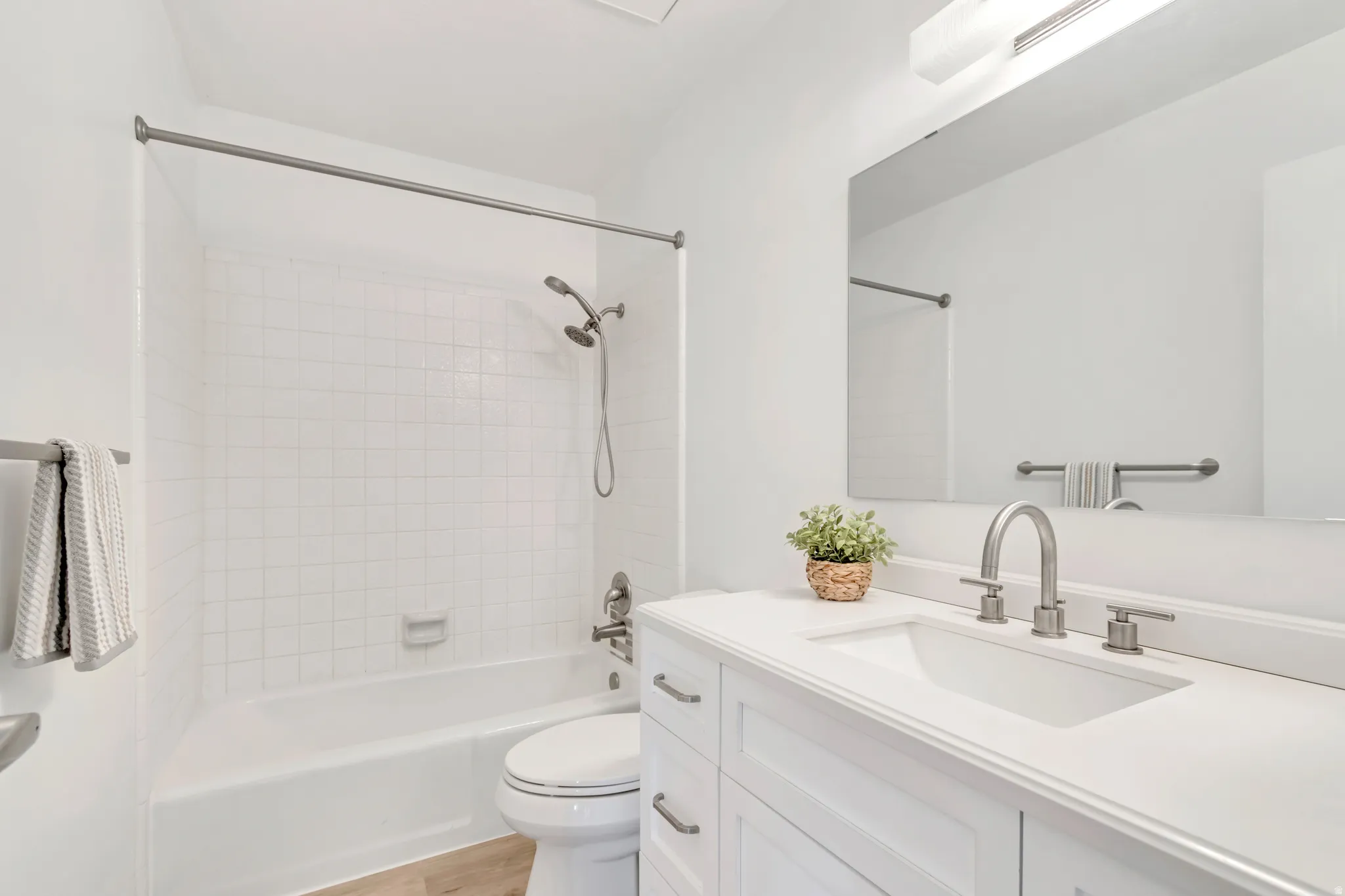 Bathroom featuring a white vanity with an integrated sink, brushed nickel fixtures, a full-width mirror, and a white subway-tiled tub and shower combination