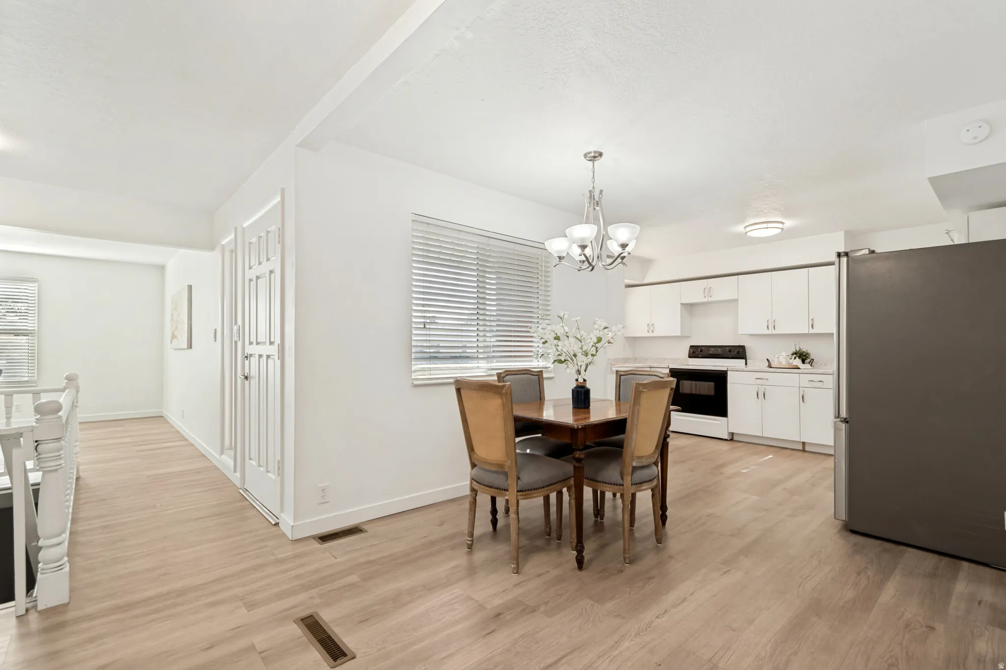 Open-concept kitchen and dining area featuring light wood-finish flooring, white cabinetry, and stainless steel appliances