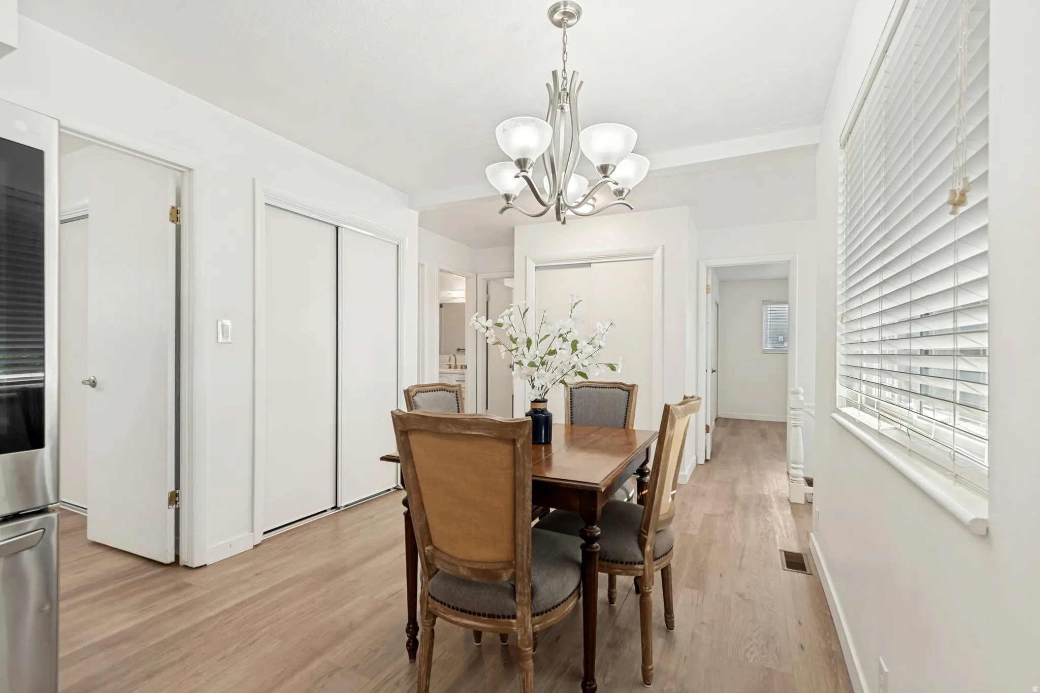 Dining area featuring light wood-finish flooring, white window blinds, and a brushed nickel chandelier