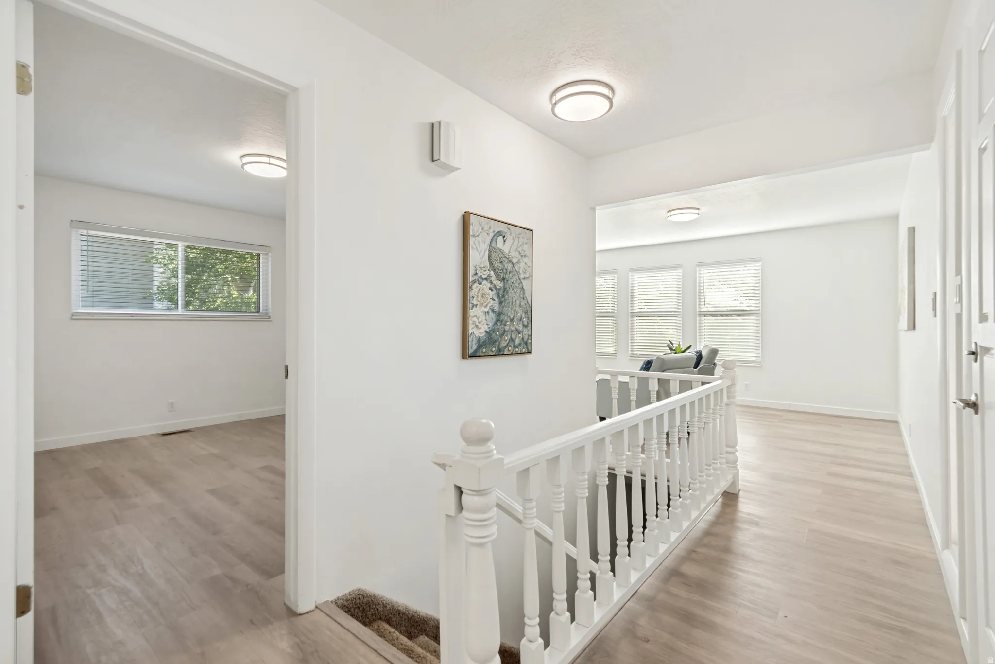 Hallway featuring light wood-finish flooring, white walls, and a white balustrade