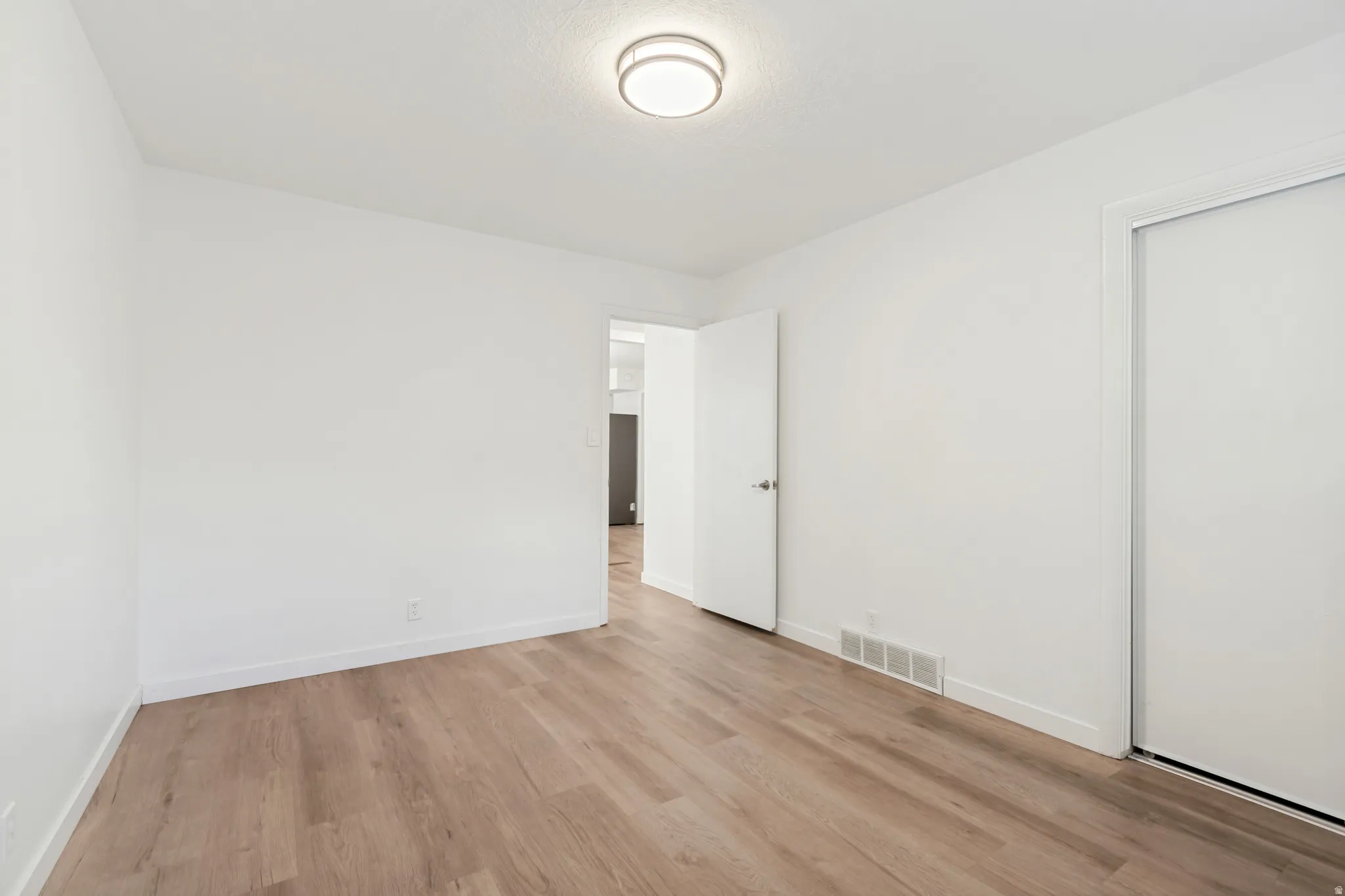 Bright room with wood-finish flooring, white walls, and a contemporary flush-mount ceiling light