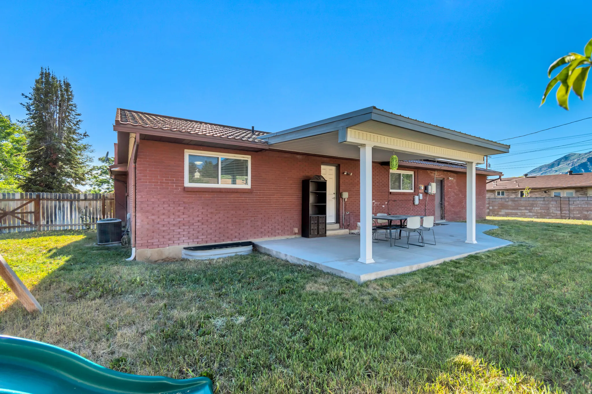 Red brick exterior featuring a covered patio with white support columns, a concrete patio surface, and a fenced backyard