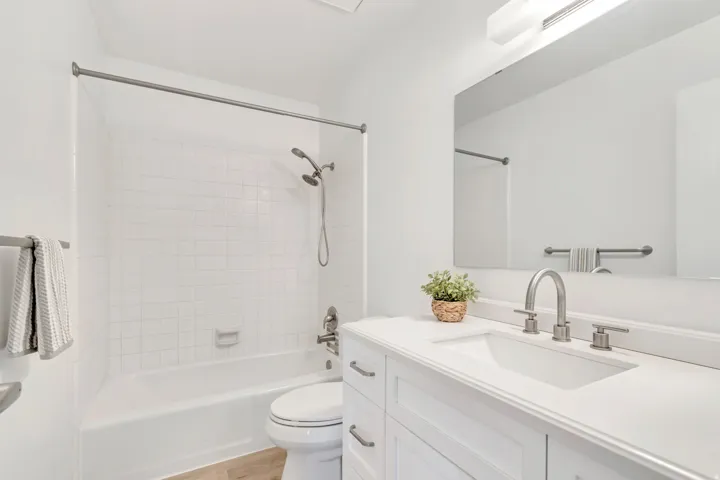 Bathroom featuring a white vanity with an integrated sink, brushed nickel fixtures, a full-width mirror, and a white subway-tiled tub and shower combination