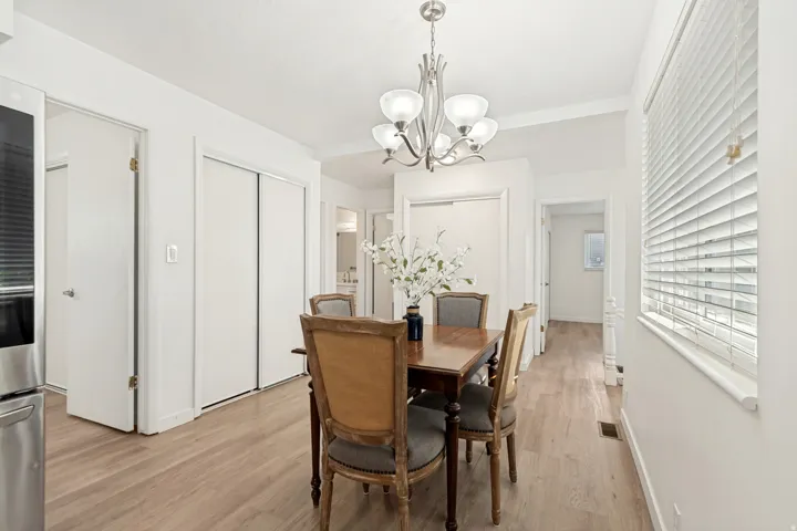 Dining area featuring light wood-finish flooring, white window blinds, and a brushed nickel chandelier
