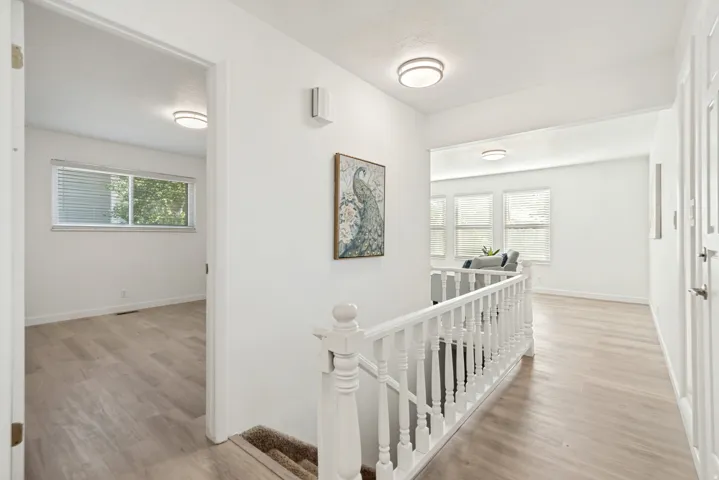 Hallway featuring light wood-finish flooring, white walls, and a white balustrade