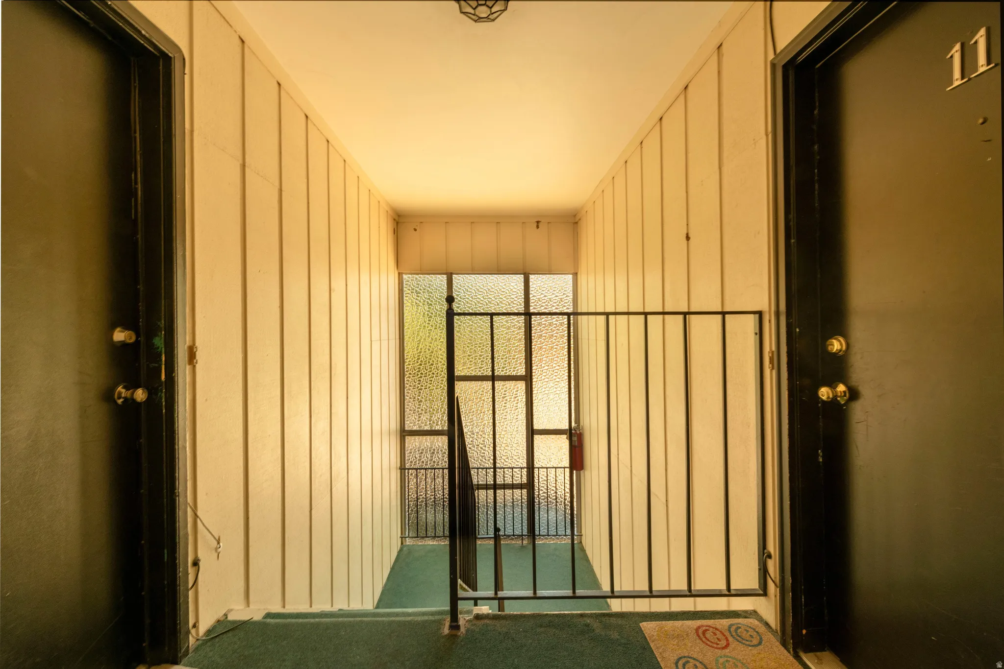Corridor featuring paneling walls, green carpeting, and dark entry doors with brass hardware