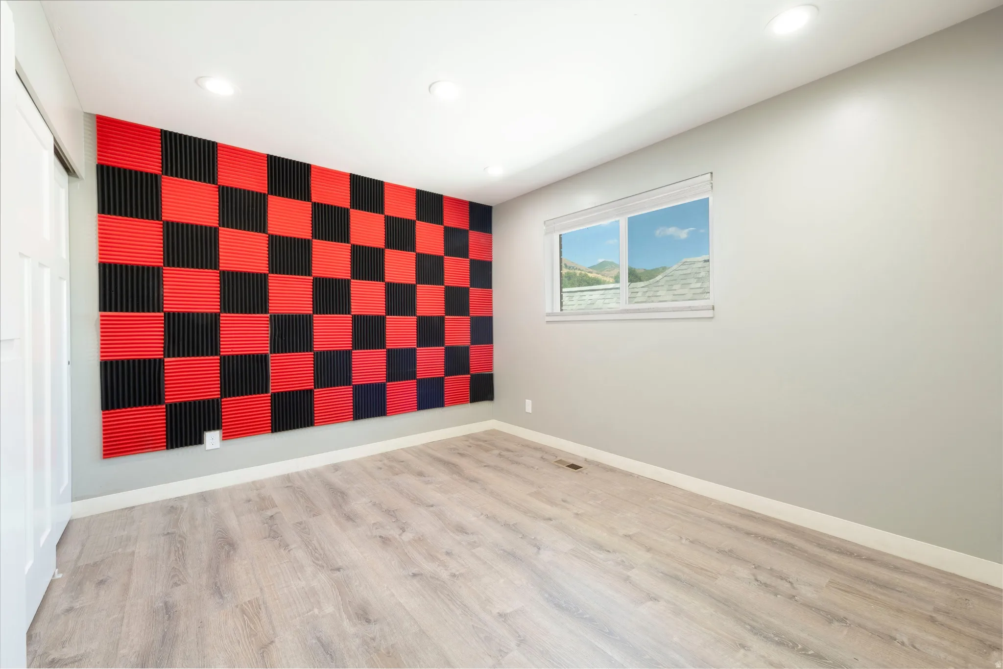 Accent wall with red and black acoustic paneling, complemented by light wood-finish flooring