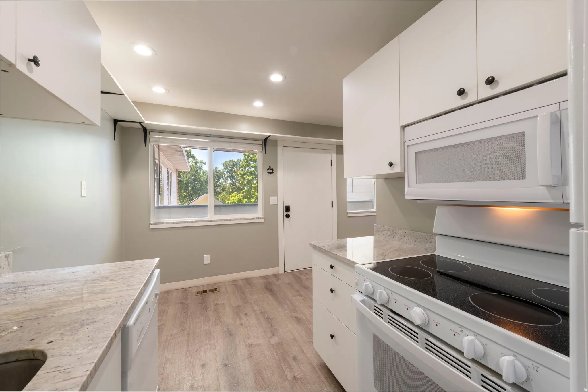 Kitchen featuring white cabinetry with dark hardware, a built-in microwave, and a white electric range with a black cooktop