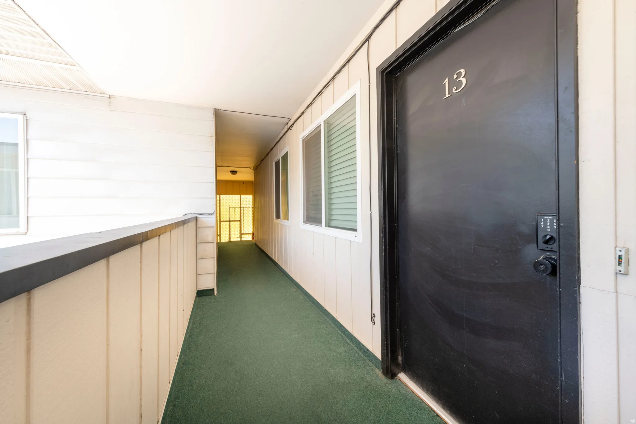 Entryway featuring a black door with modern keyless entry, visible house number, and a green carpeted walkway