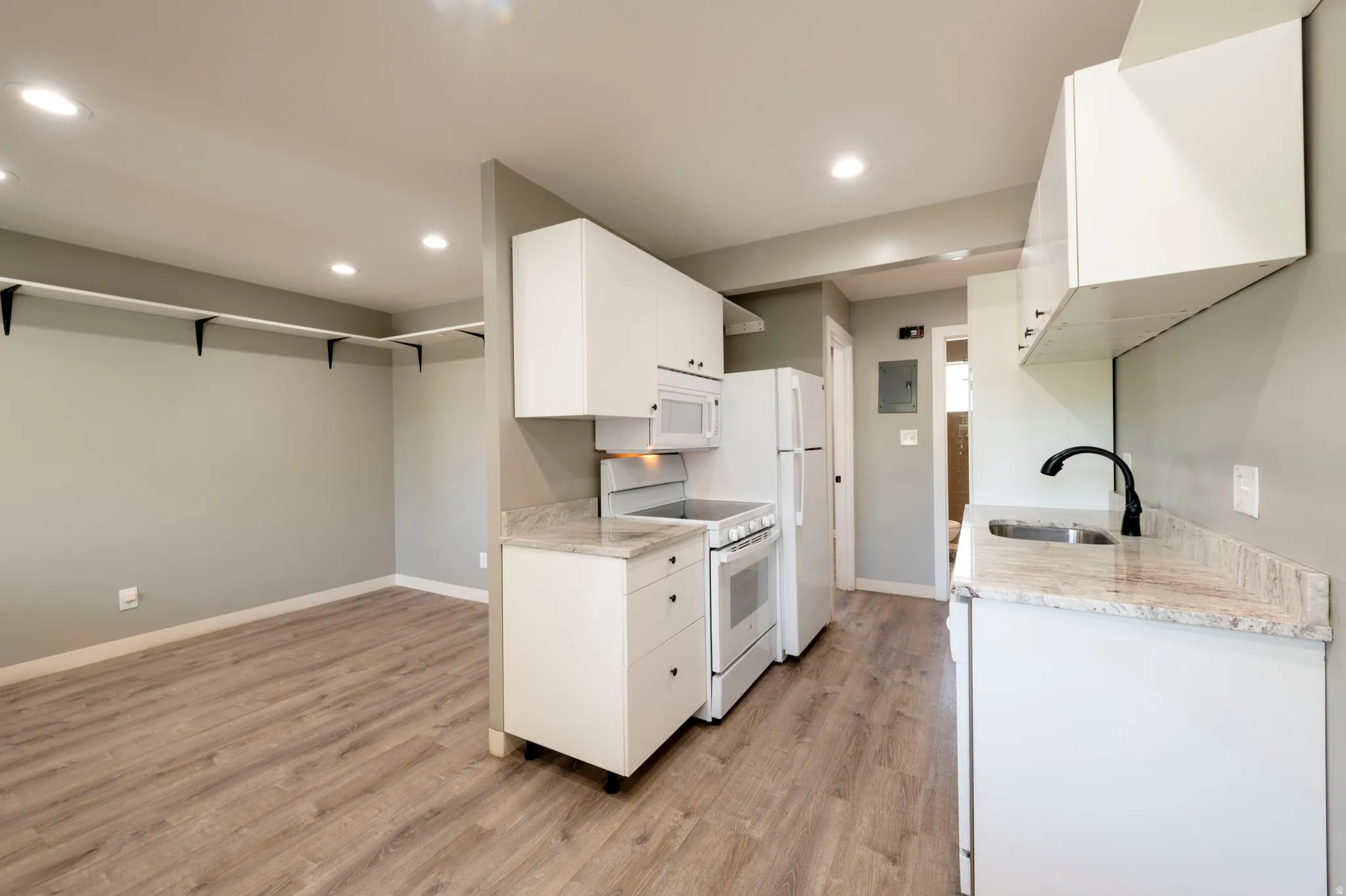 Compact kitchen featuring white cabinetry, stone-look countertops, and white appliances including a refrigerator, range, and microwave