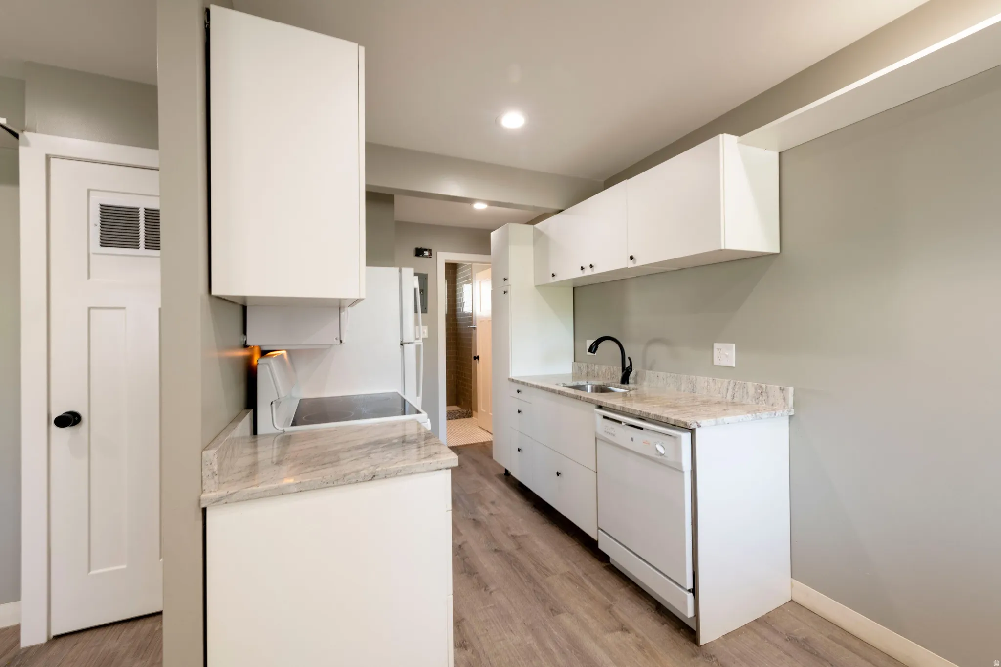 Contemporary kitchen featuring white cabinetry, light-toned countertops, integrated sink with a matte black faucet, and wood-finish flooring