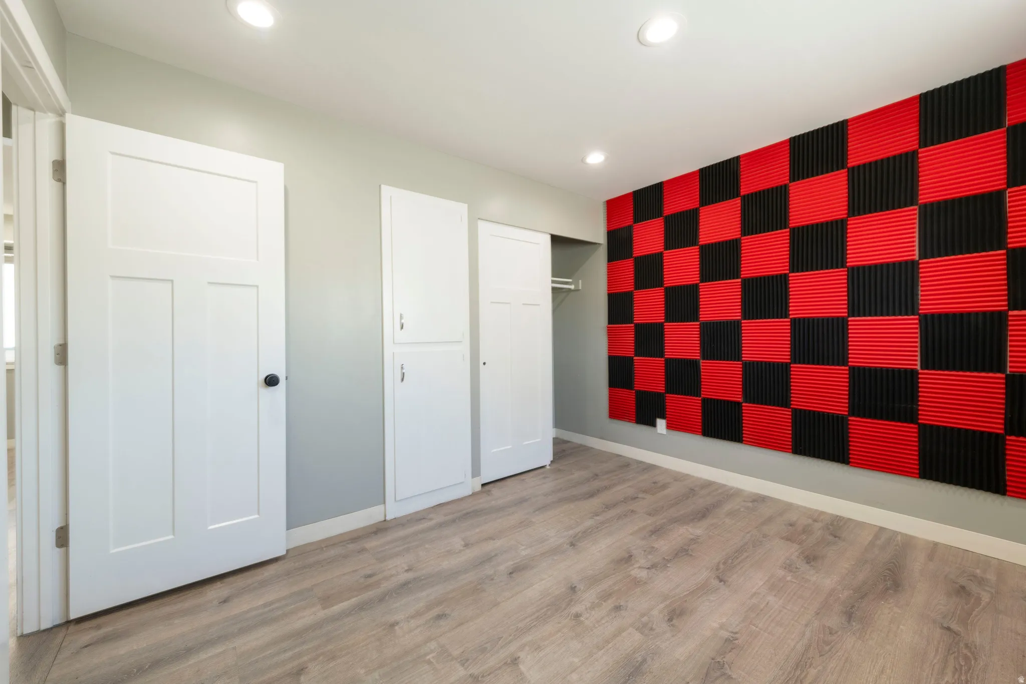 Open room featuring wood-finish flooring, recessed lighting, and a checkered red and black acoustic panel wall