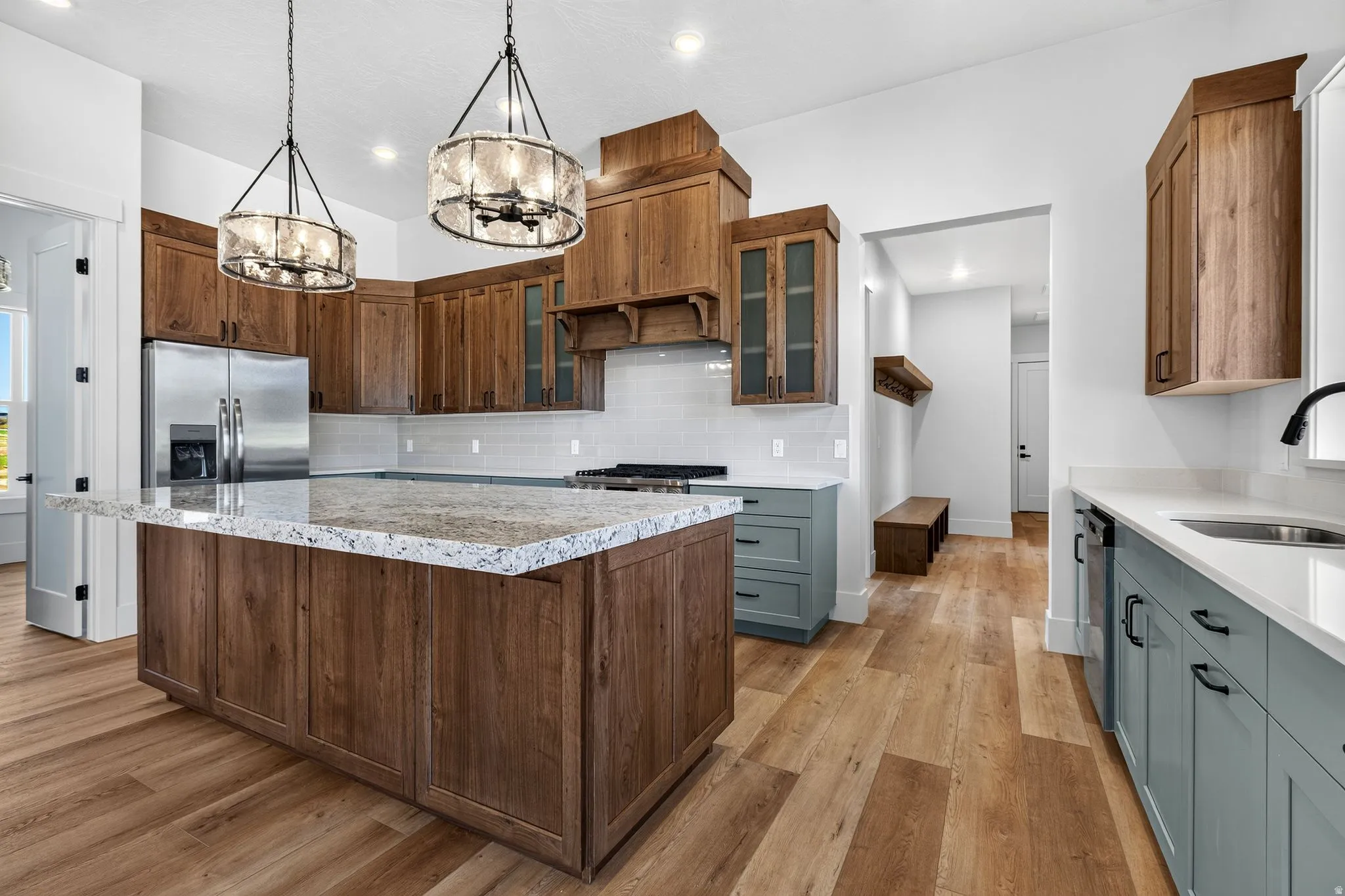 Open-concept kitchen featuring a large central island with a light-colored countertop, laminate flooring, two decorative pendant light fixtures, stainless steel appliances, and a tiled backsplash