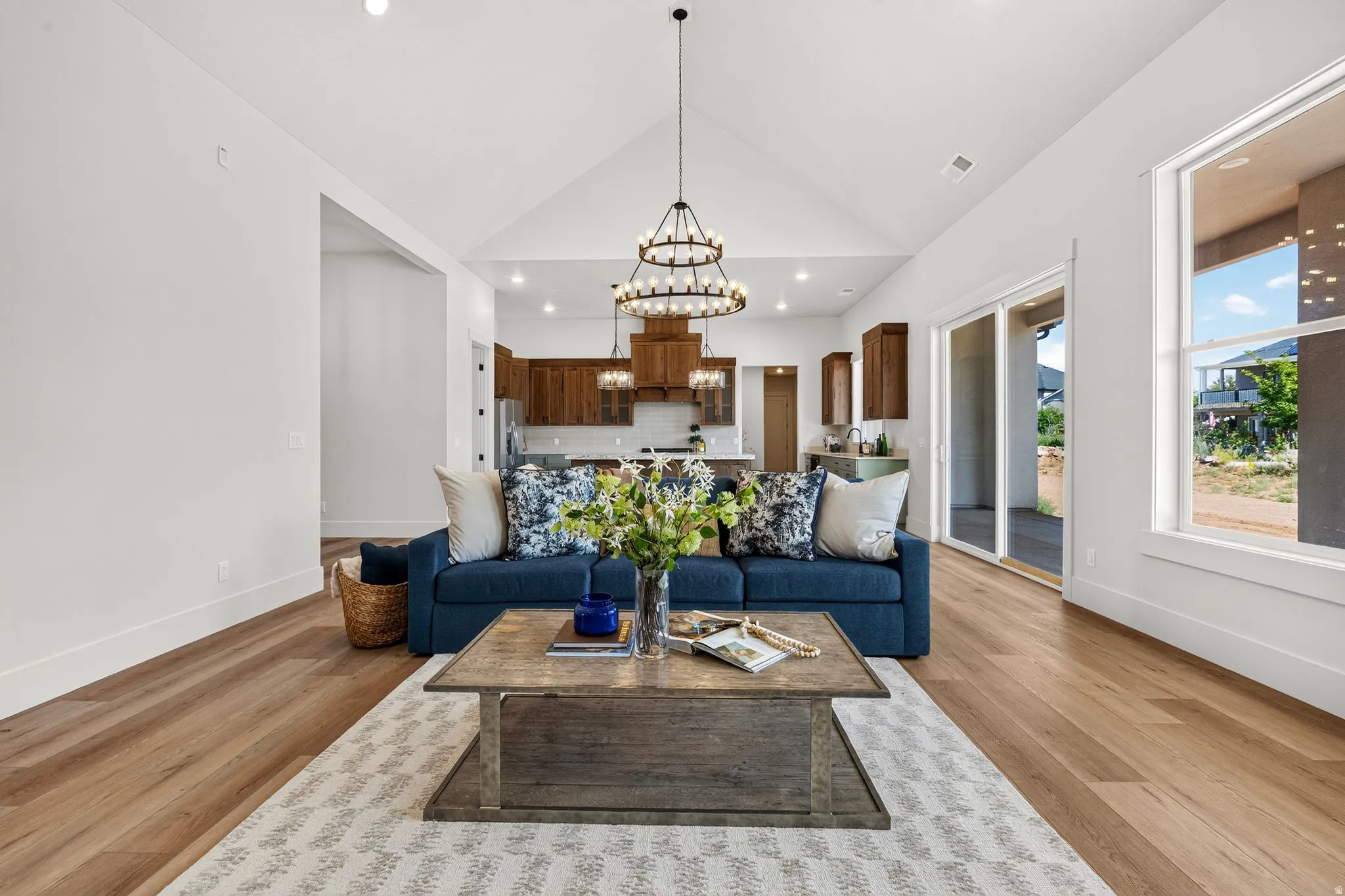 Vaulted ceiling living space featuring wood-finish flooring, a contemporary chandelier, large windows, and sliding glass doors