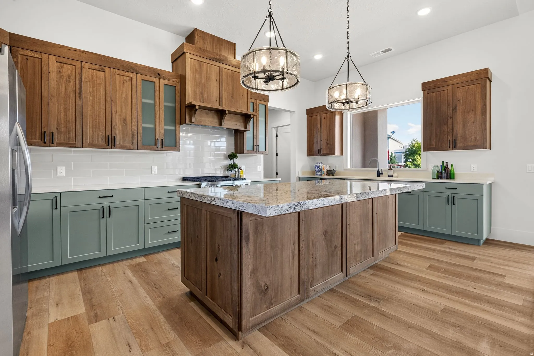 Spacious kitchen featuring a large central island with a stone countertop, wood-finish flooring, two-tone cabinetry, and pendant lighting