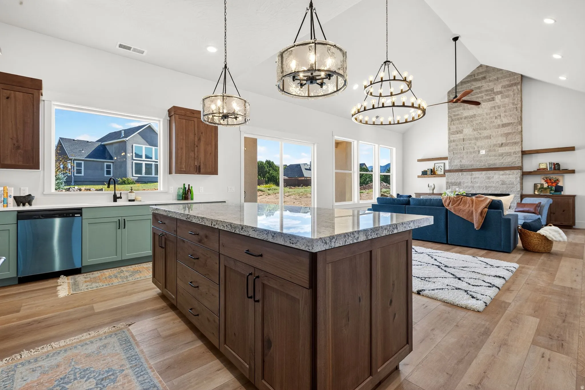 Open-concept kitchen and living area featuring a large center island with a light-toned countertop, wood-finish flooring, and vaulted ceilings