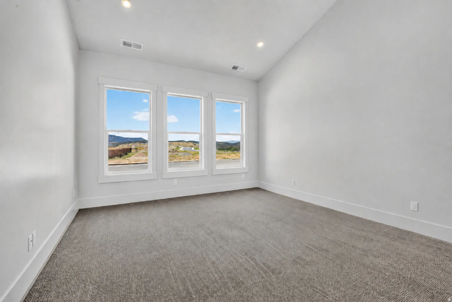 Primary bedroom with three large windows showcasing a distant mountain range and vaulted ceiling