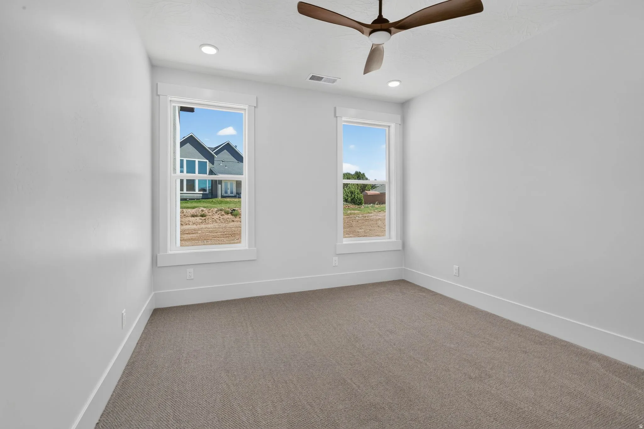 Spacious bedroom featuring neutral carpeting, white walls, two large windows with white trim, a modern ceiling fan, and recessed lighting