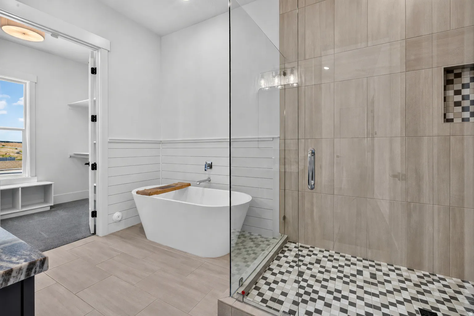 Spacious primary ensuite featuring a freestanding soaking tub, a large glass-enclosed shower with contrasting floor tile, a built-in shower niche, and tile flooring