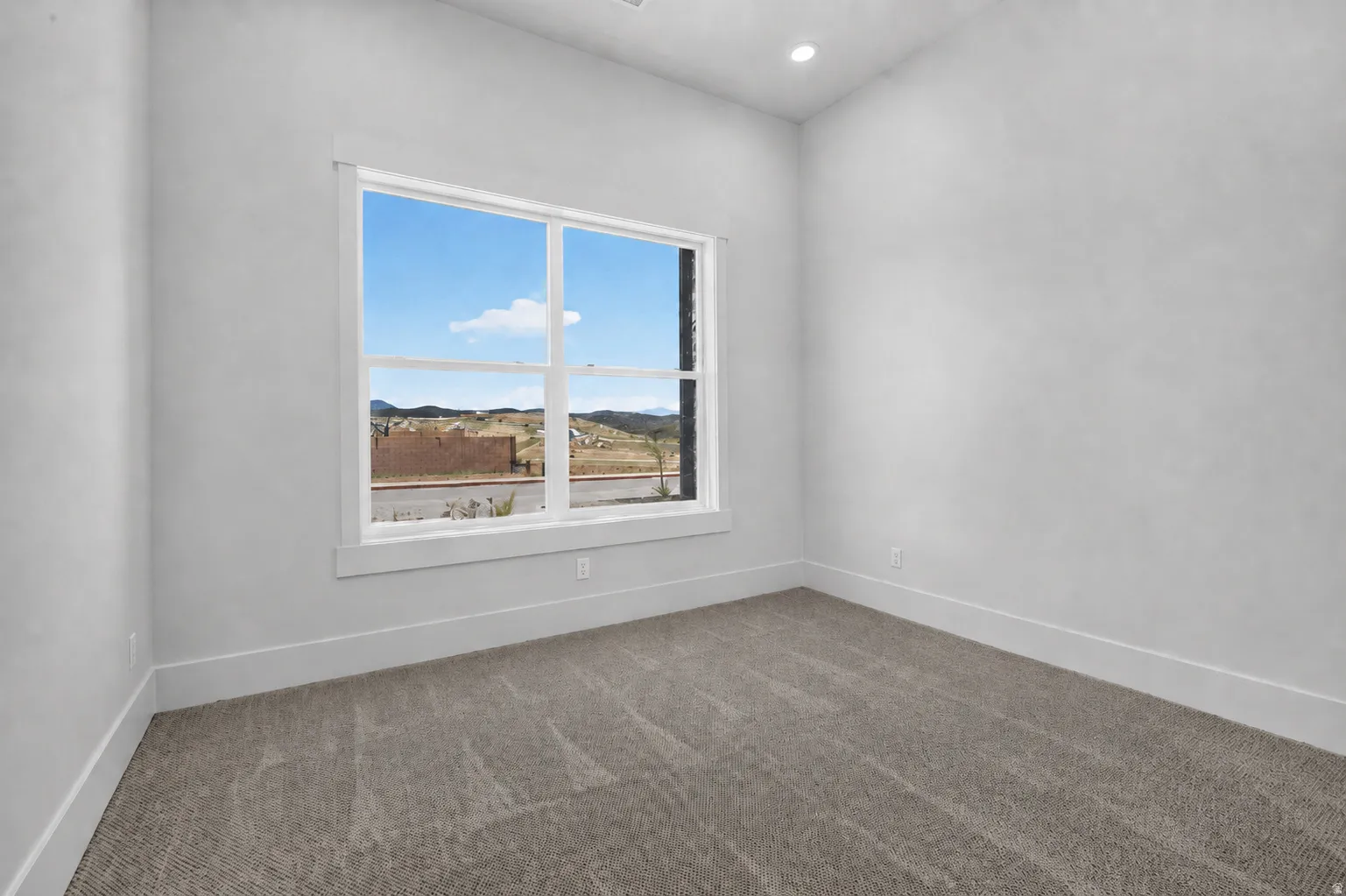 Spacious  bedroom featuring a large window with white trim, gray carpeted flooring, white walls, and a recessed ceiling light