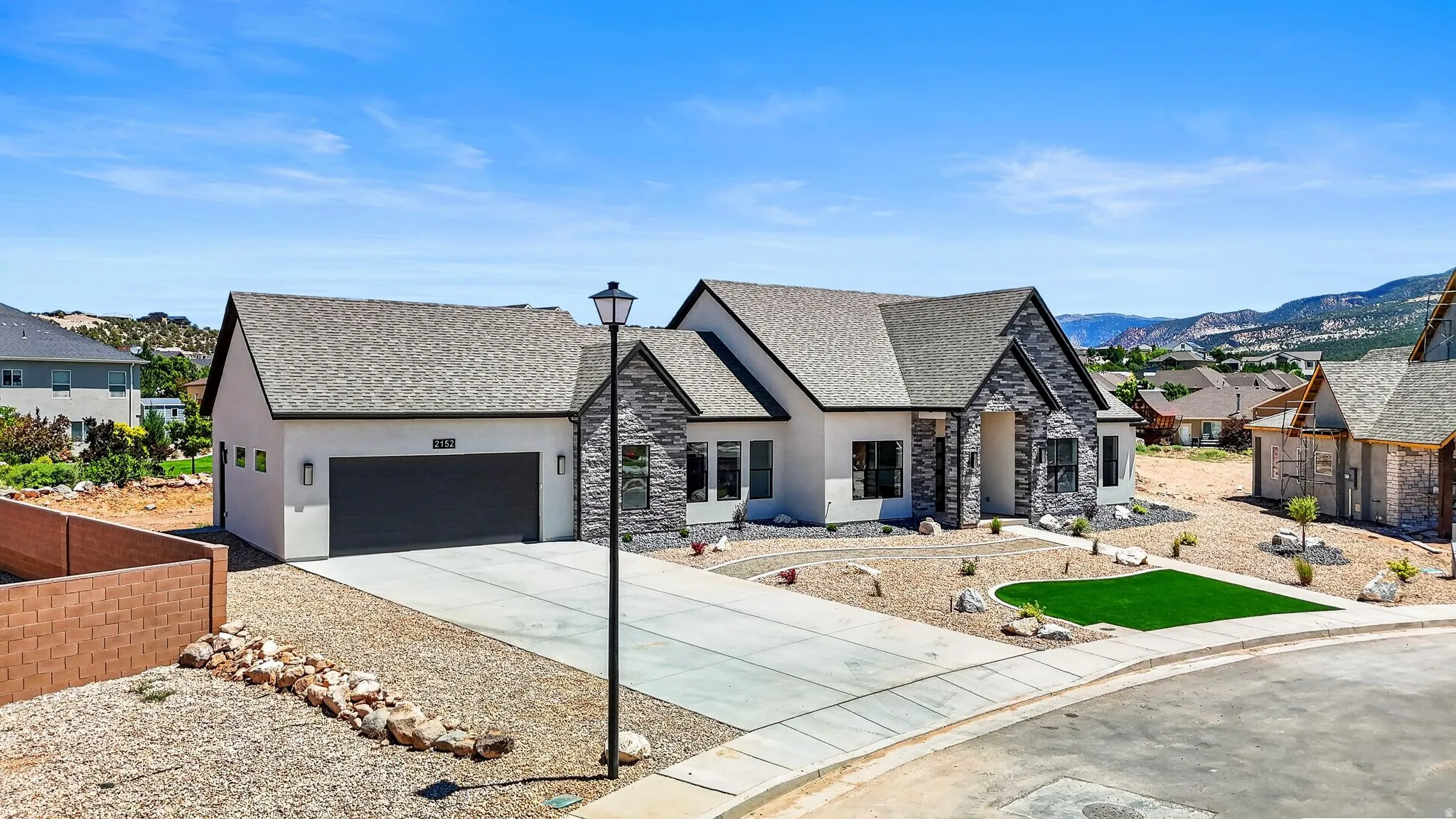 Contemporary residence featuring a blend of white stucco and dark stone veneer, a deep gray garage door, and a light gray shingle roof