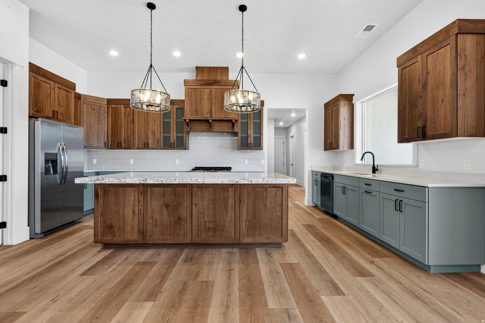 Spacious kitchen featuring a large central island with a light-toned countertop, laminate flooring, and a mix of wood-toned and sage green cabinetry