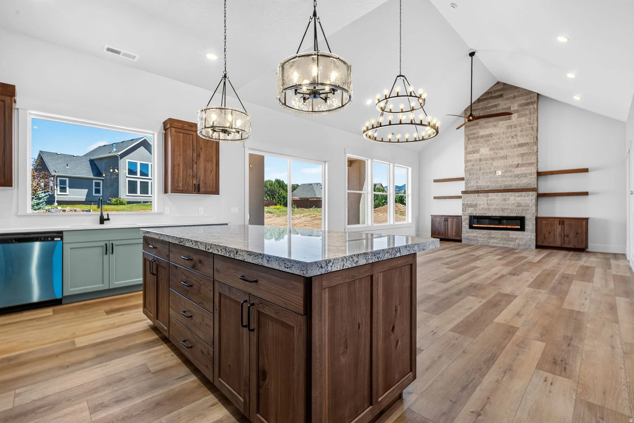 Open-concept living space with vaulted ceilings, laminate flooring, and a stone-clad fireplace featuring an electric insert