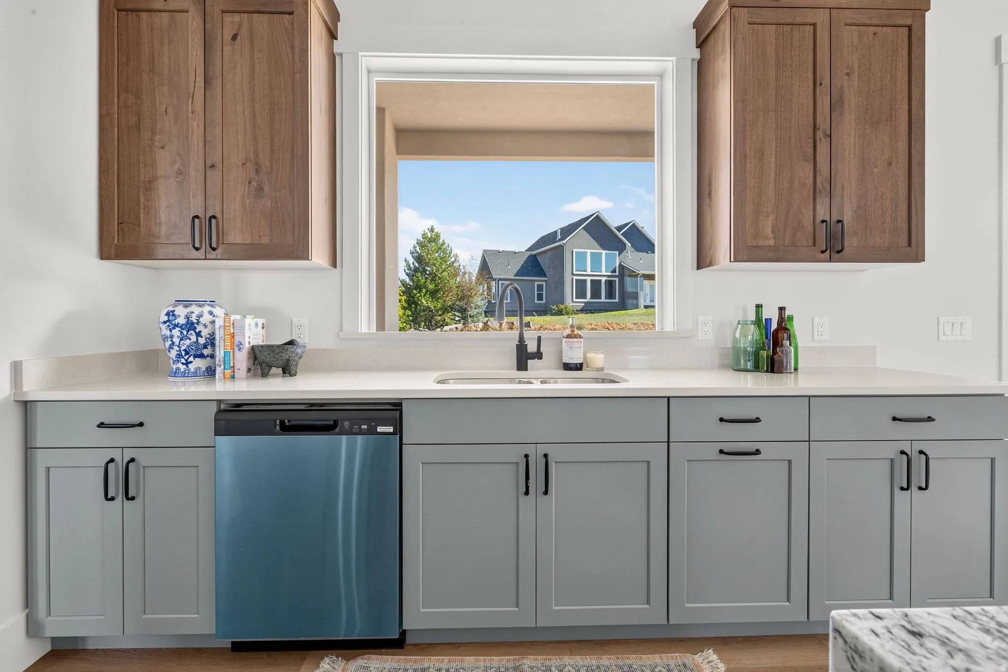 Contemporary kitchen sink area featuring a black faucet, stainless steel dishwasher, light gray lower cabinetry, and wood-finish upper cabinetry