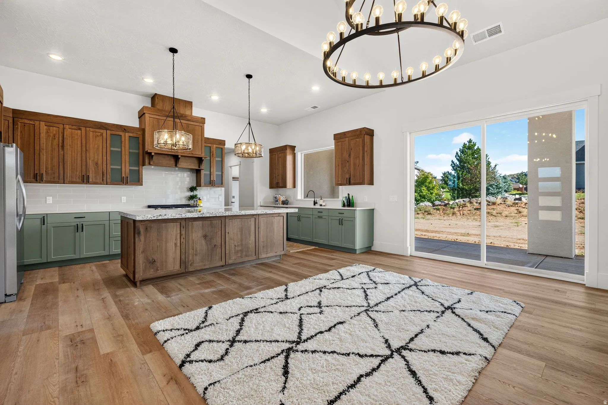 Open-concept kitchen featuring wood-finish flooring, a central island with a light-toned countertop, and two-tone cabinetry with wood-finish upper cabinets and sage green lower cabinets