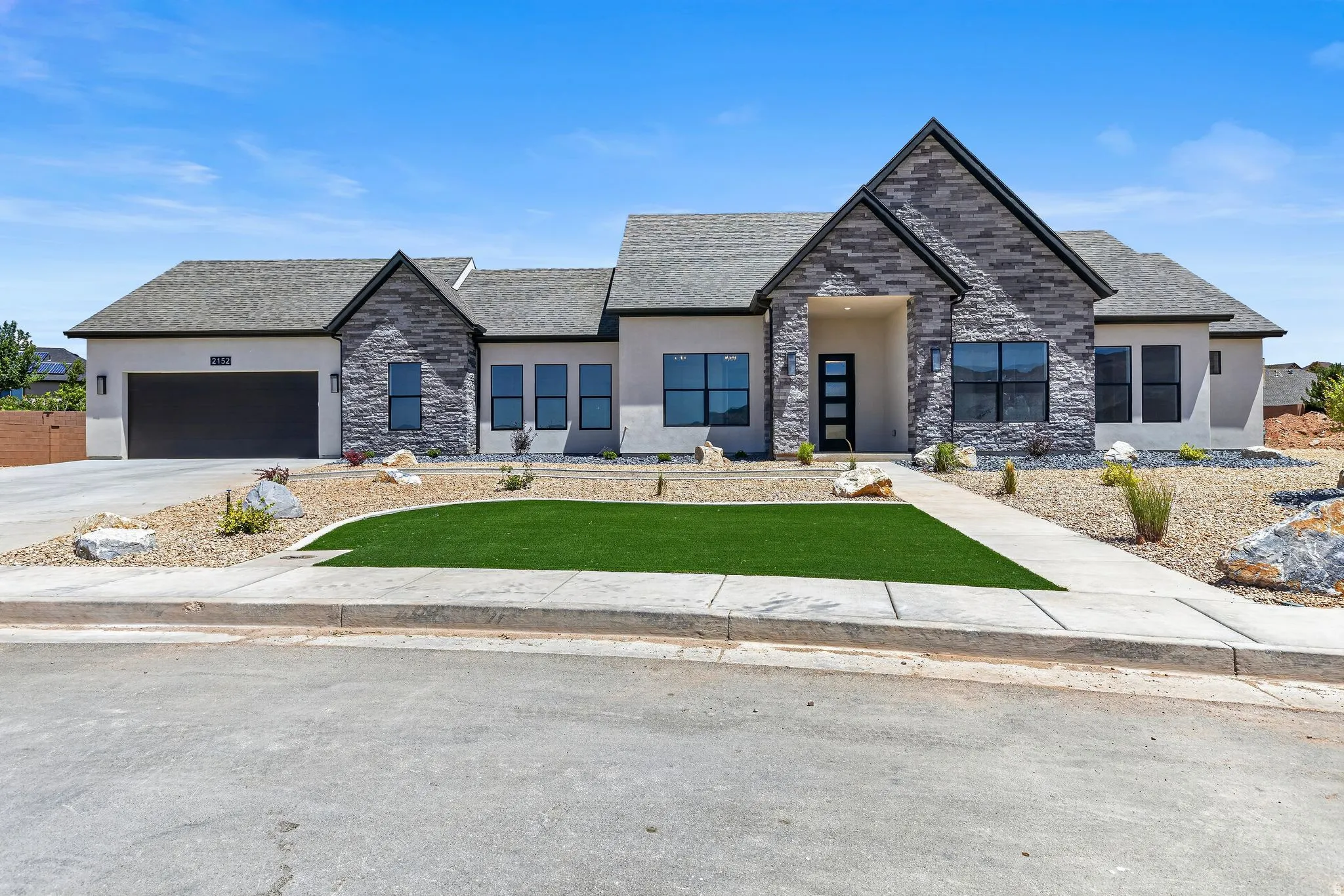 Contemporary stucco and stone exterior featuring a dark gray shingled roof and a prominent gable