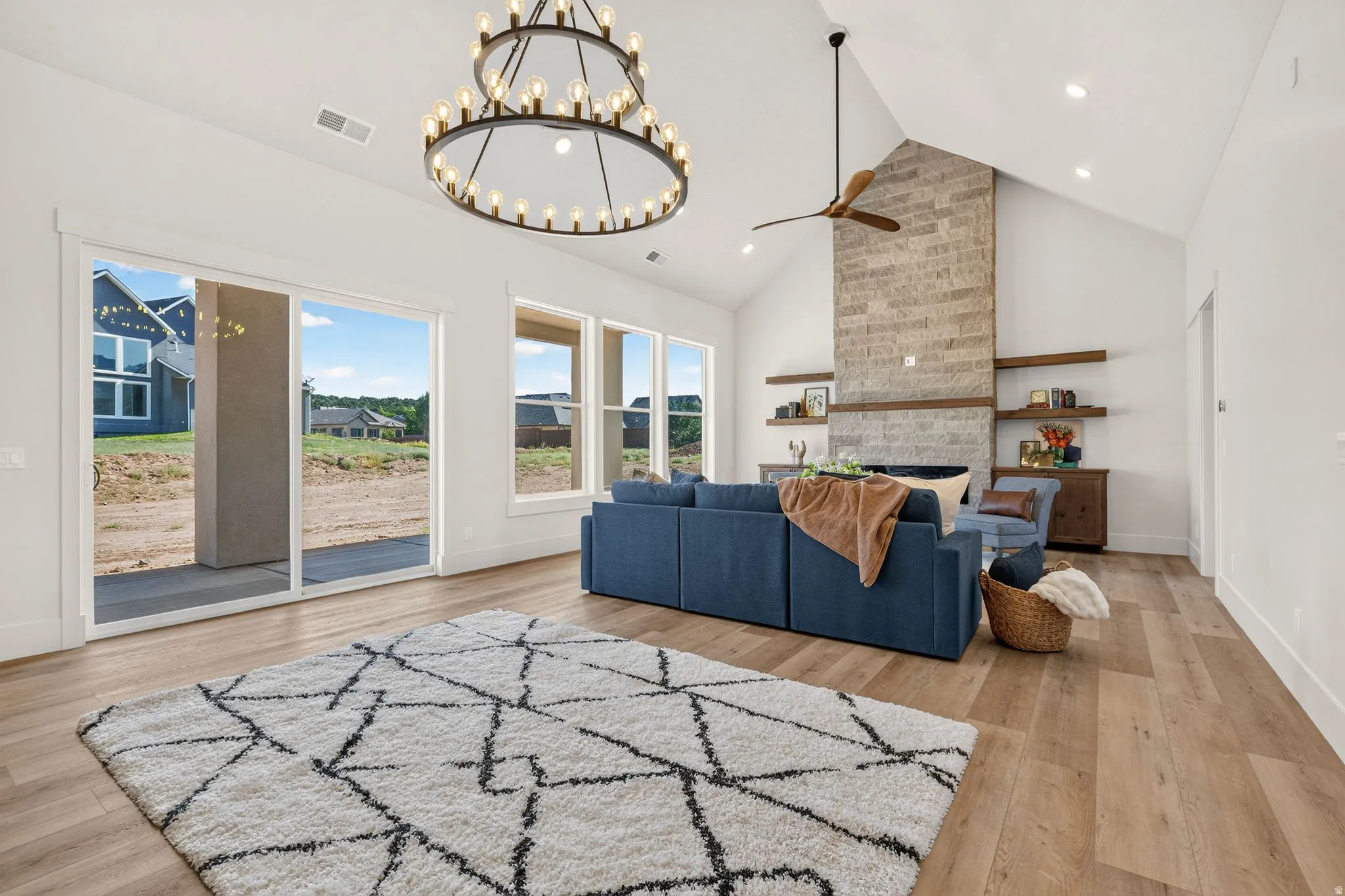 Spacious living area featuring high vaulted ceilings, light wood-finish flooring, and a stone-clad fireplace with built-in wooden shelving
