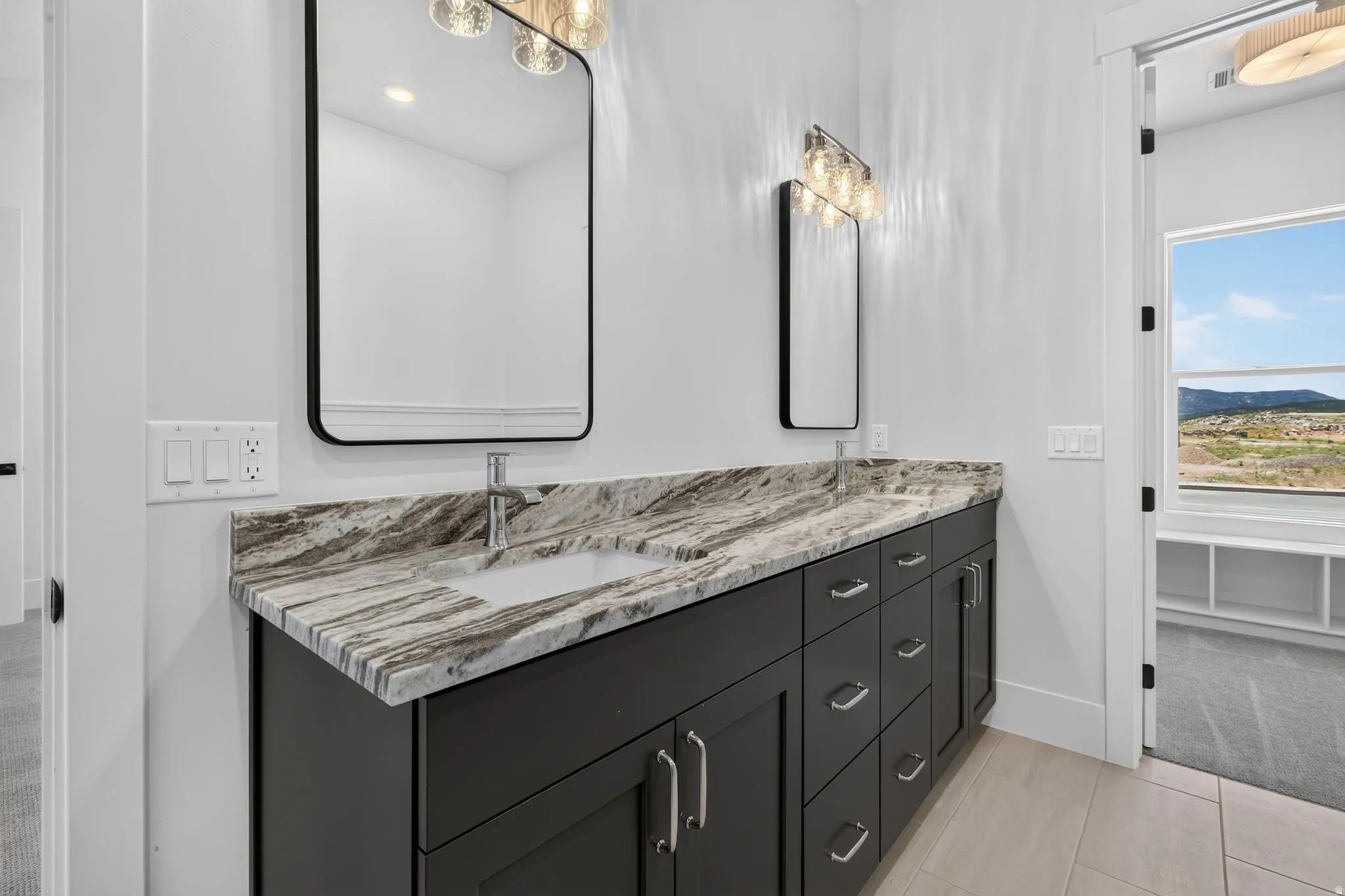 Primary ensuite. Dual vanity with gray cabinetry and stone countertops and tile flooring. Walk-in closet.
