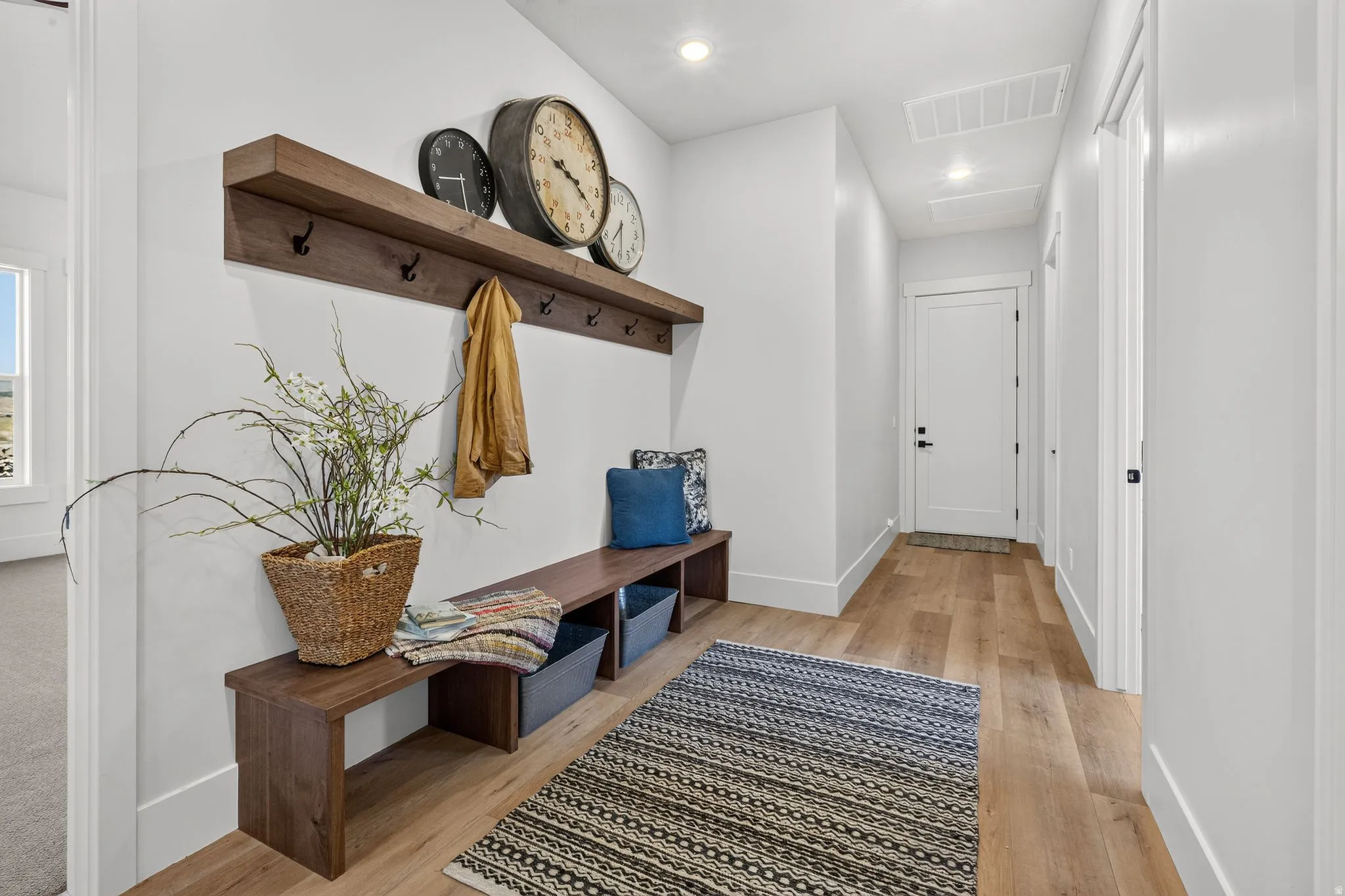 Entryway featuring wood-finish flooring, a built-in wooden bench with storage compartments, and a wall-mounted wooden shelf with coat hooks