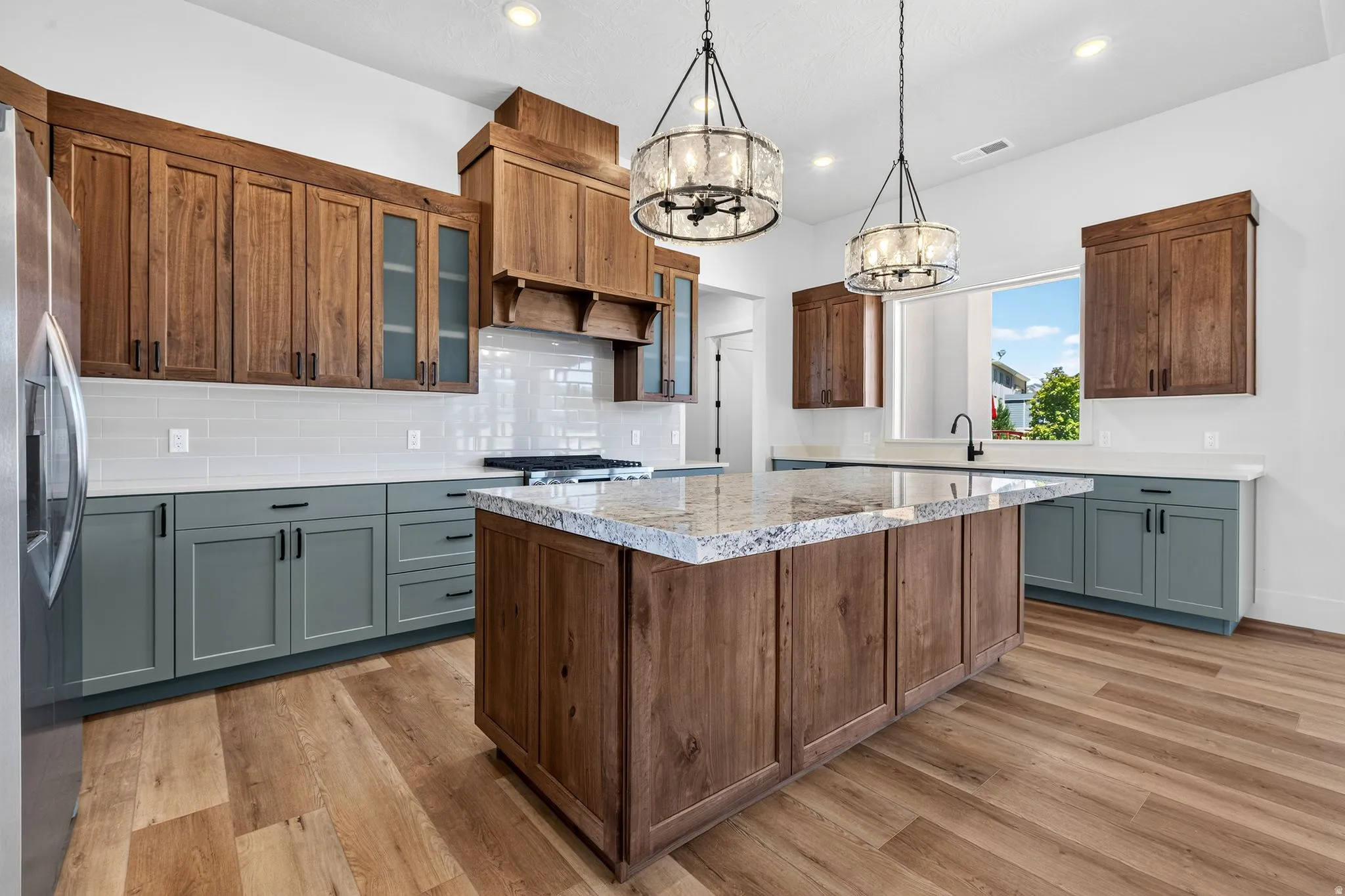 Kitchen featuring laminate flooring, a central island with a light-toned countertop, two-tone cabinetry, a tile backsplash, and contemporary pendant lighting