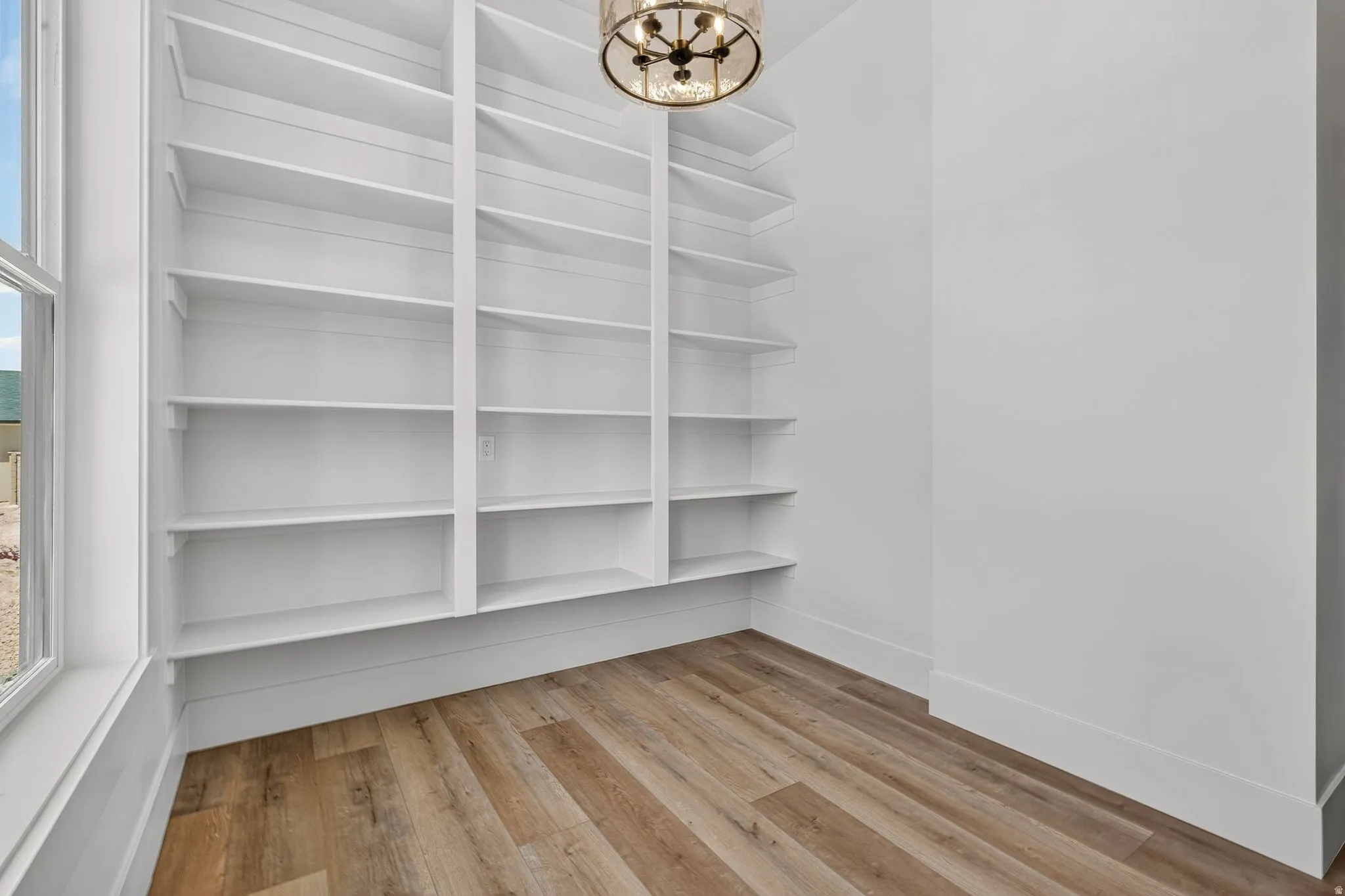 Walk-in oversized butler's pantry. Built-in white shelving providing ample storage, laminate flooring, a contemporary ceiling fixture, and a large window providing natural light