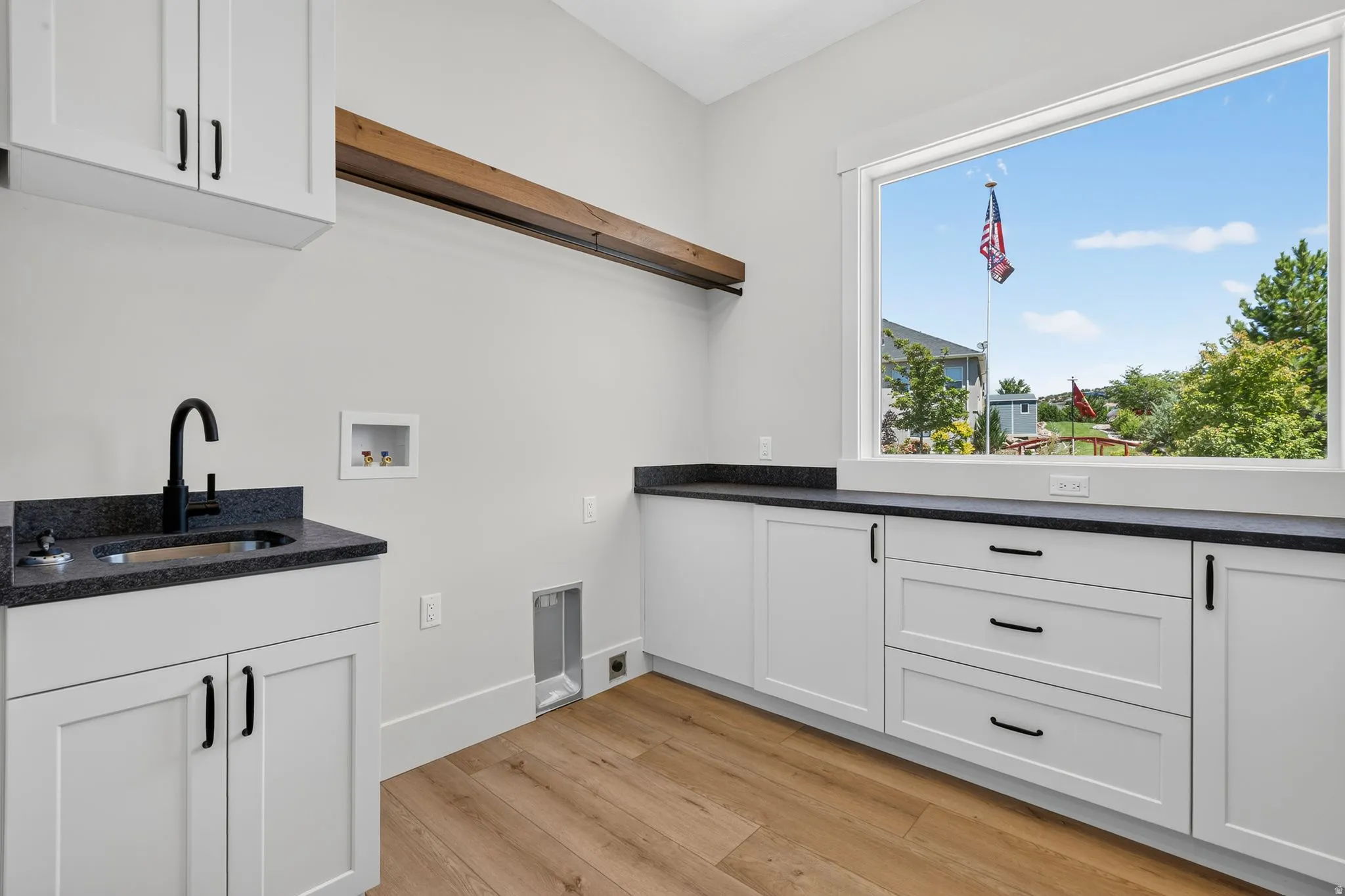 Laundry room featuring shaker cabinetry with black hardware, dark stone-finish countertops, and laminate flooring