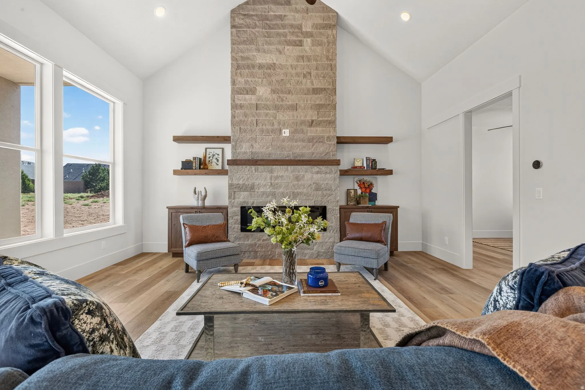 Living area featuring a stone-clad fireplace with wood mantle, vaulted ceilings, and wood-finish flooring
