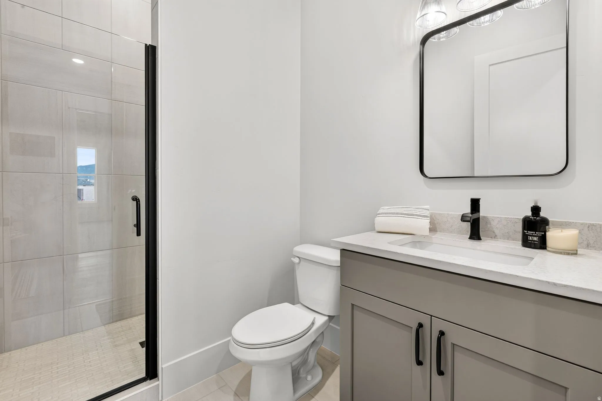 Contemporary bathroom featuring a glass-enclosed shower with tiled walls and flooring, a single-sink vanity with a light-toned countertop, and a sleek black-framed mirror
