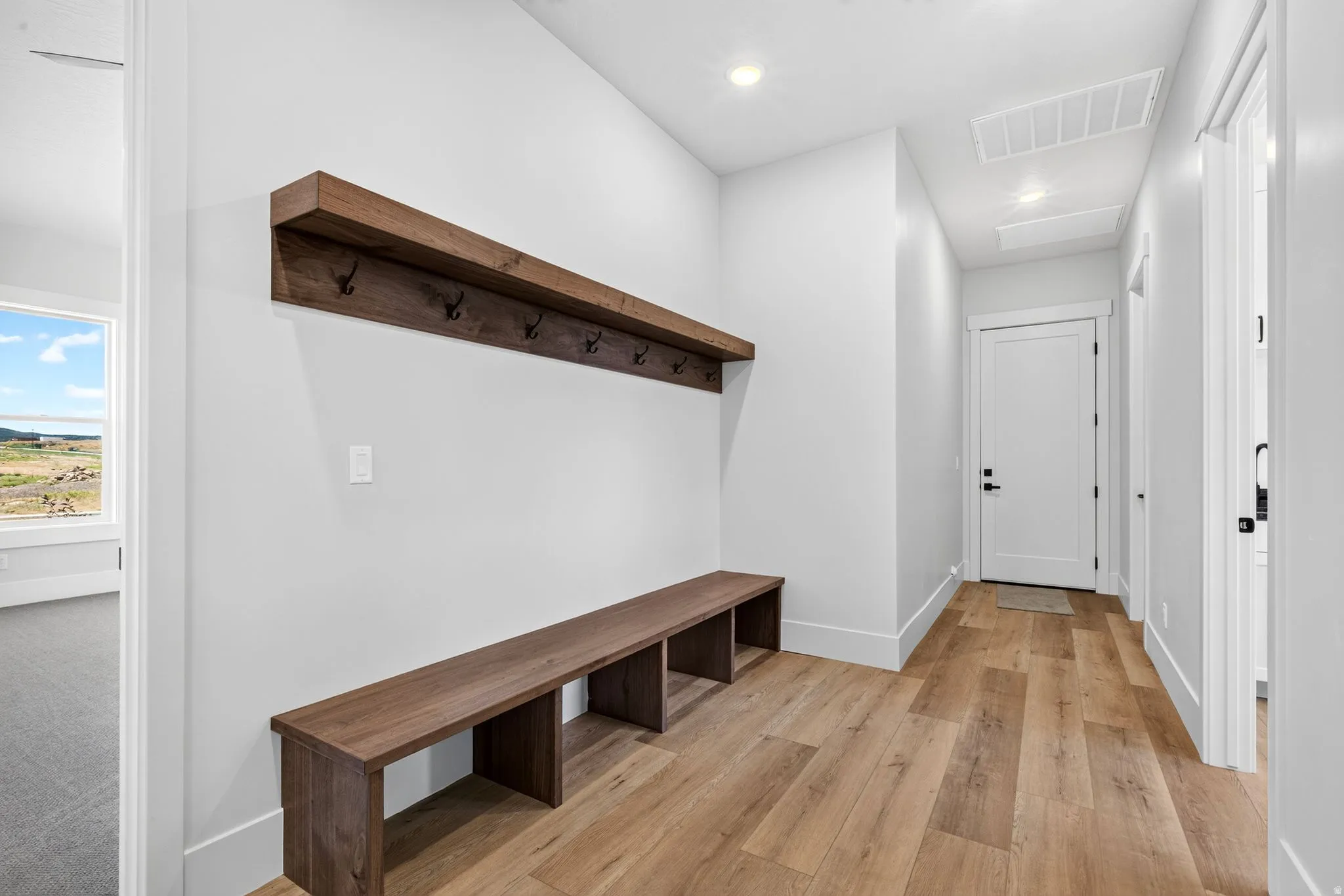 Entryway featuring laminate flooring, a built-in wood bench, and a coordinating wood shelf with dark-finish coat hooks