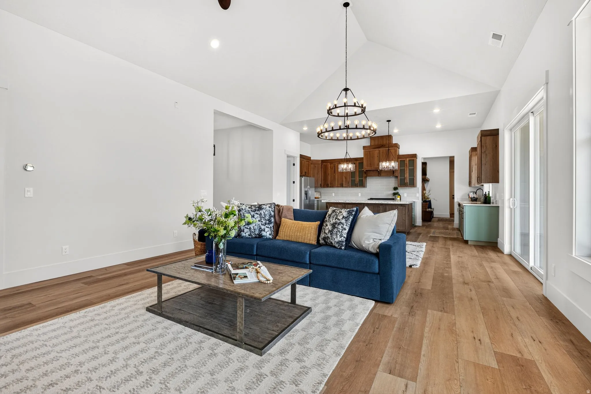Expansive living area featuring vaulted ceilings, wood-finish flooring, a contemporary chandelier, and a sliding glass door