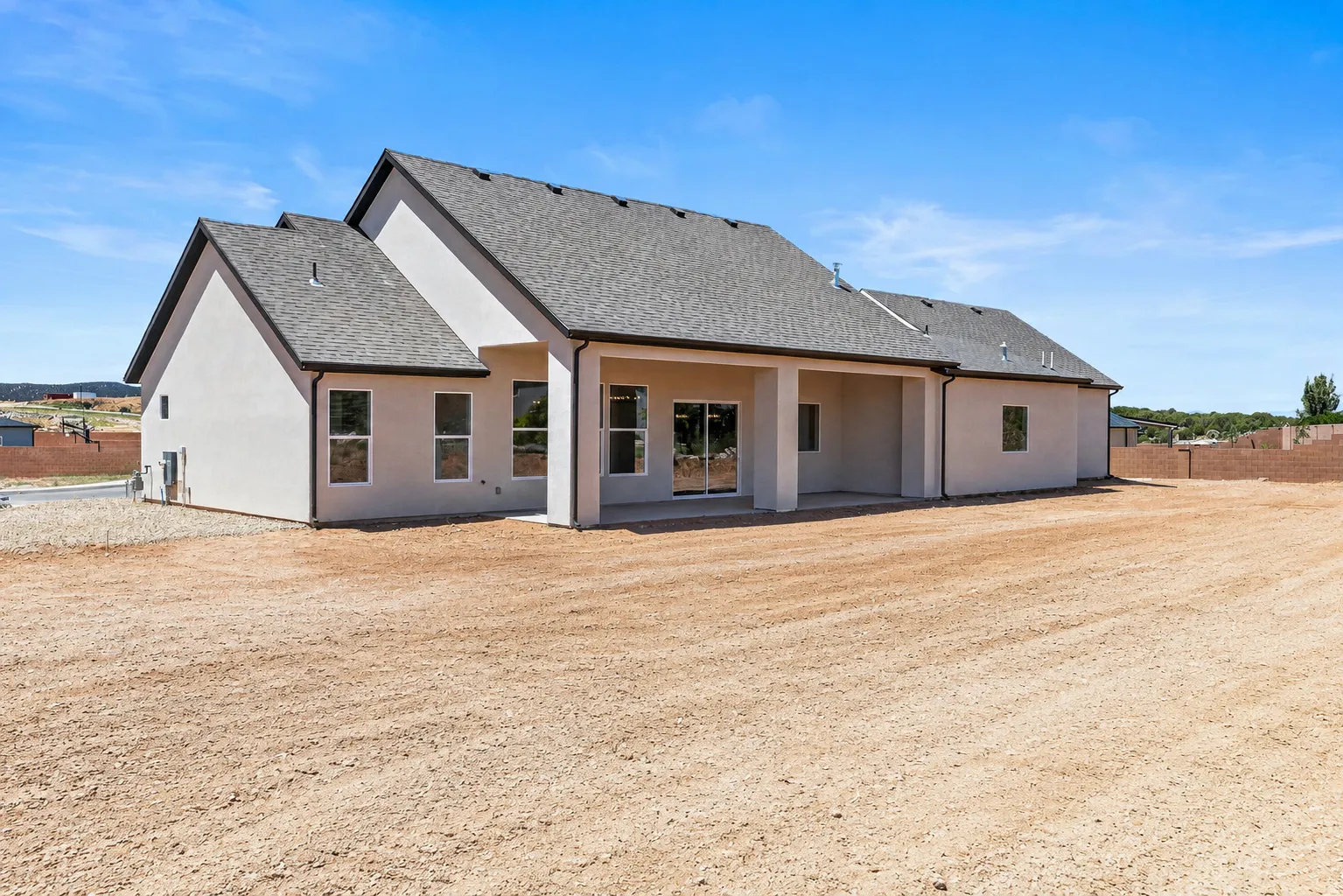 Contemporary stucco exterior with a covered patio, multiple rear windows, and a spacious graded lot