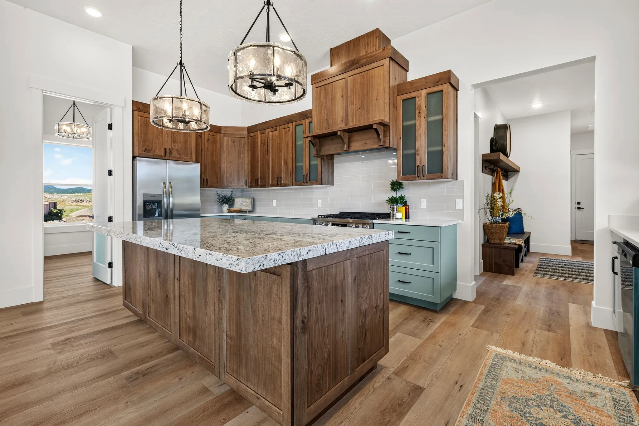 Spacious kitchen featuring a large island with a light-toned countertop, wood-finish flooring, and two modern drum pendant lights