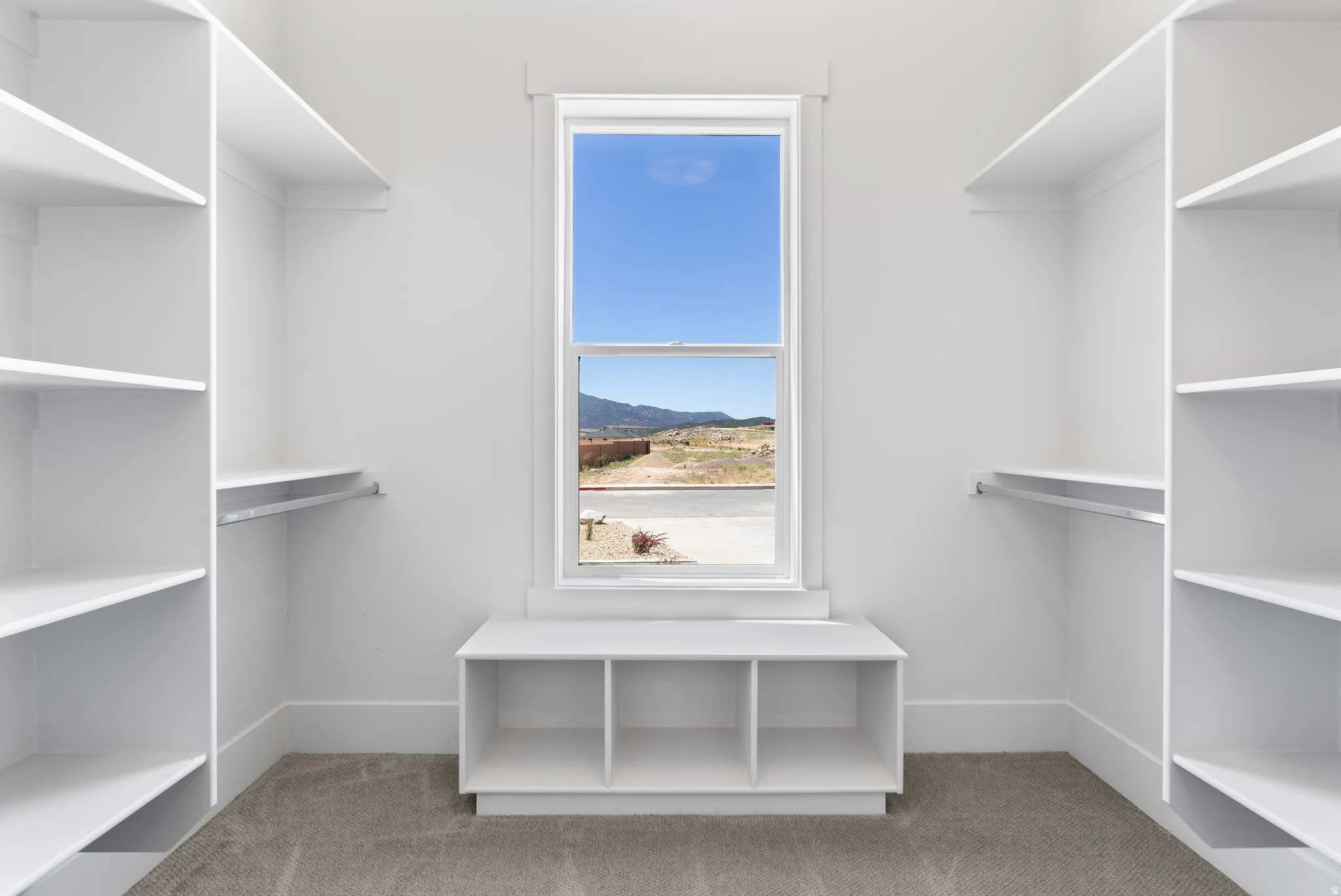 Walk-in primary ensuite closet featuring extensive built-in shelving, hanging rods, an integrated storage bench, and a framed window