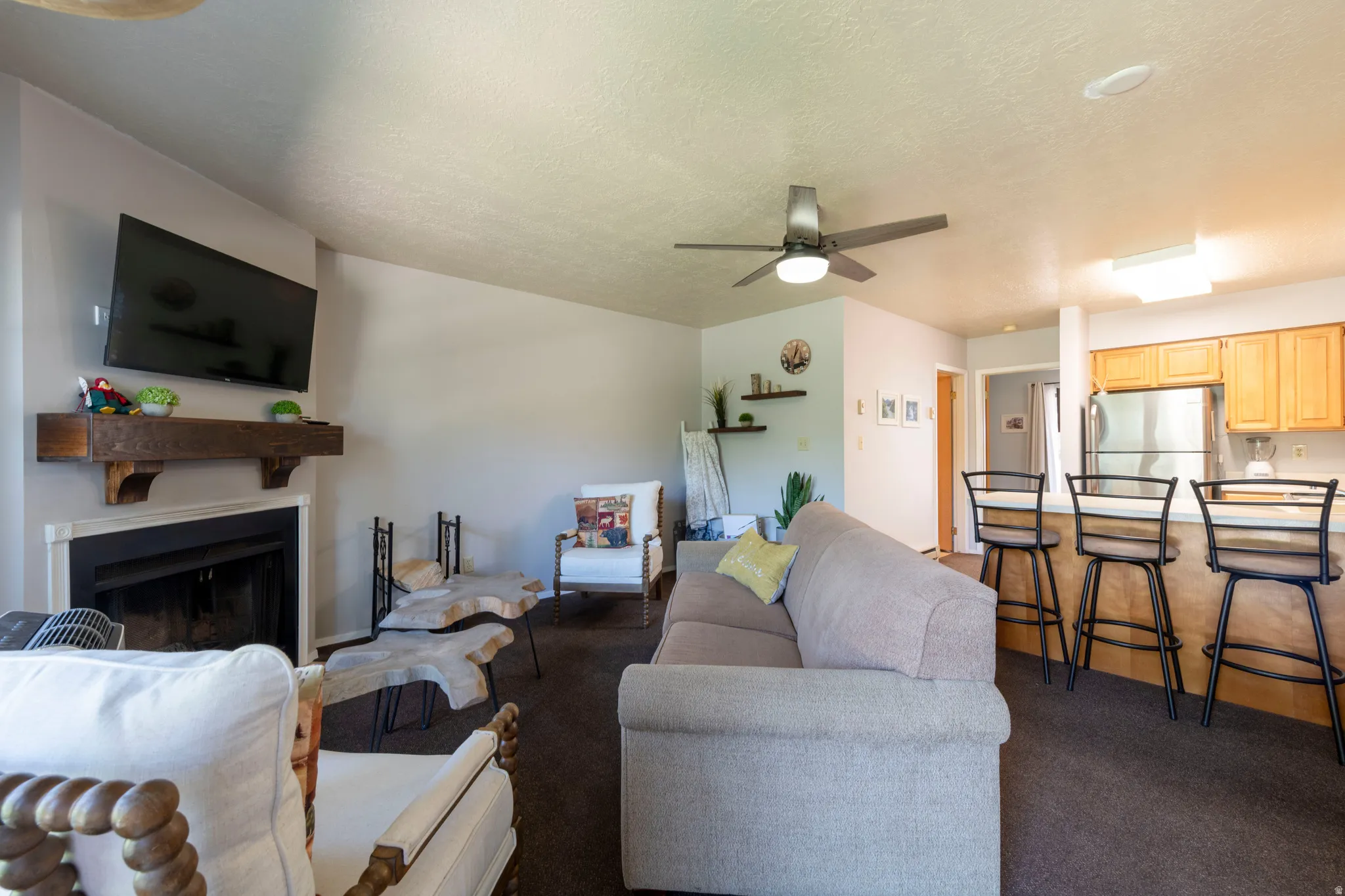 Living area featuring a fireplace with a wood mantle, ceiling fan, and carpeted flooring