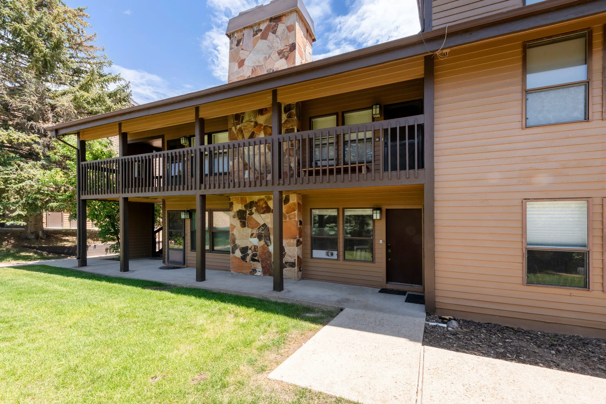Two-story exterior featuring stone veneer accents, an upper-level balcony with wood railing, and a ground-floor patio