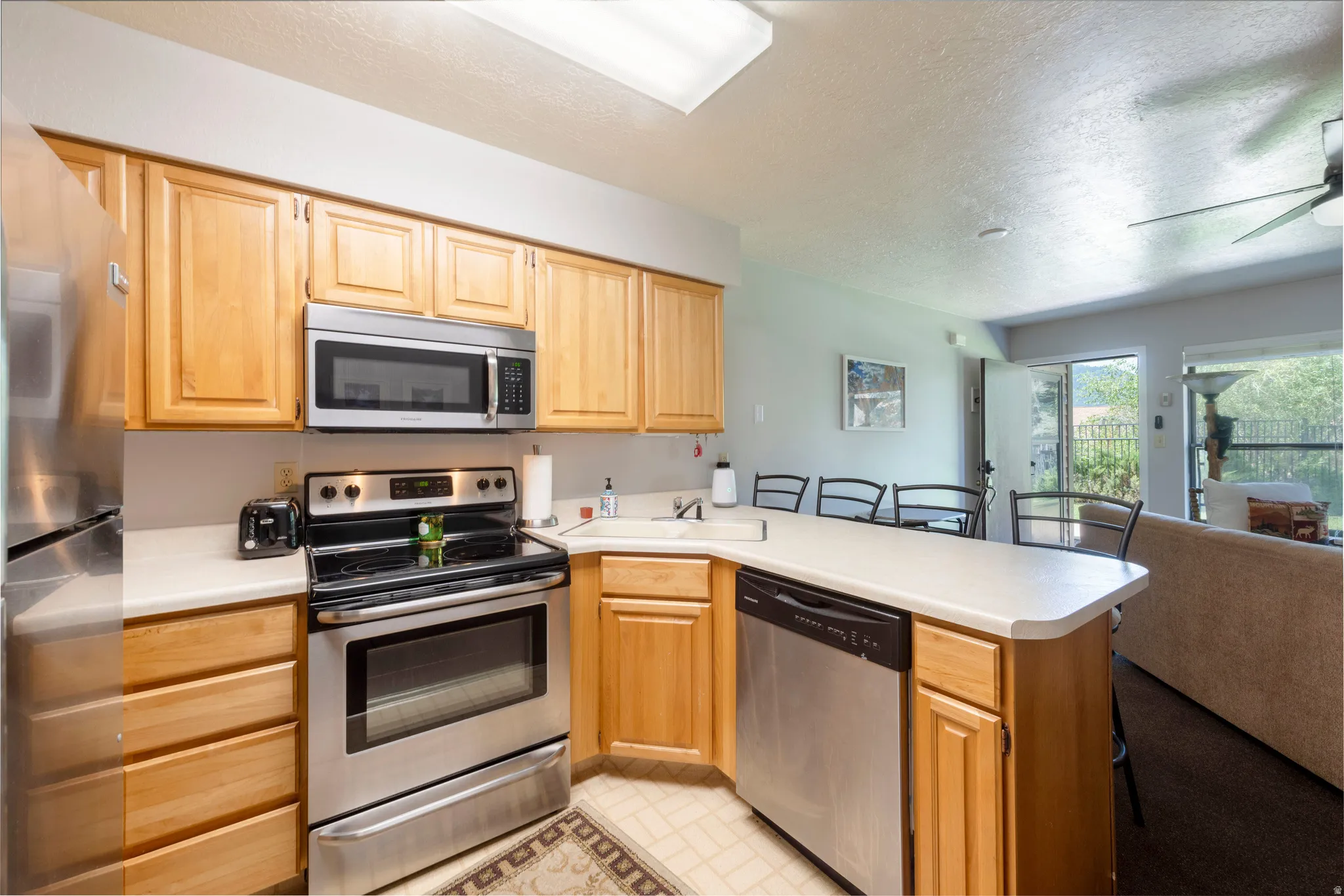 Kitchen featuring light wood cabinetry, stainless steel appliances, a white solid surface countertop, and a built-in dishwasher