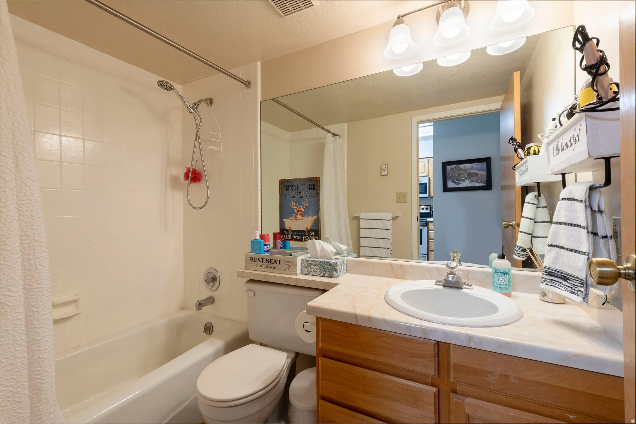 Full bathroom featuring a tub and shower combination with white tile surround, wood-finish vanity with a single basin sink, and a large wall-mounted mirror with overhead lighting