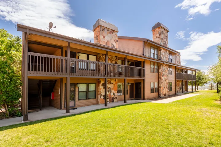 Multi-level building with stone and siding exterior, featuring multiple balconies with wood railings, exterior staircases, and a manicured lawn