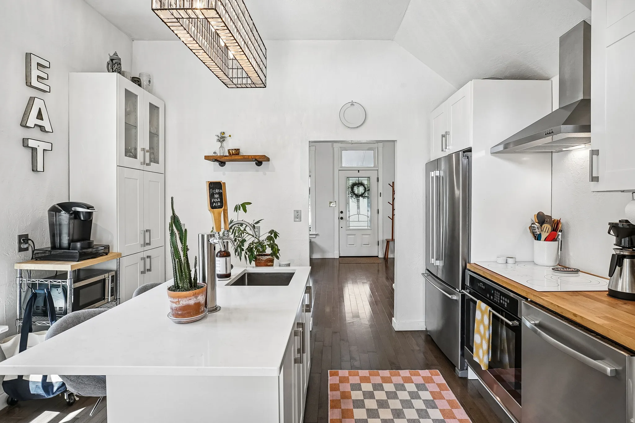 Spacious kitchen featuring an extended island with integrated sink, white cabinetry, stainless steel appliances, and wood-finish flooring