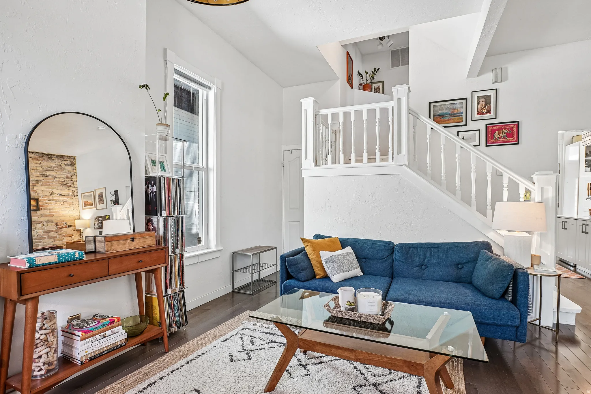 Living area featuring dark wood-finish flooring, white painted walls, and a prominent staircase with white balusters